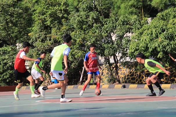 Boys playing soccer on a sunny outdoor court.