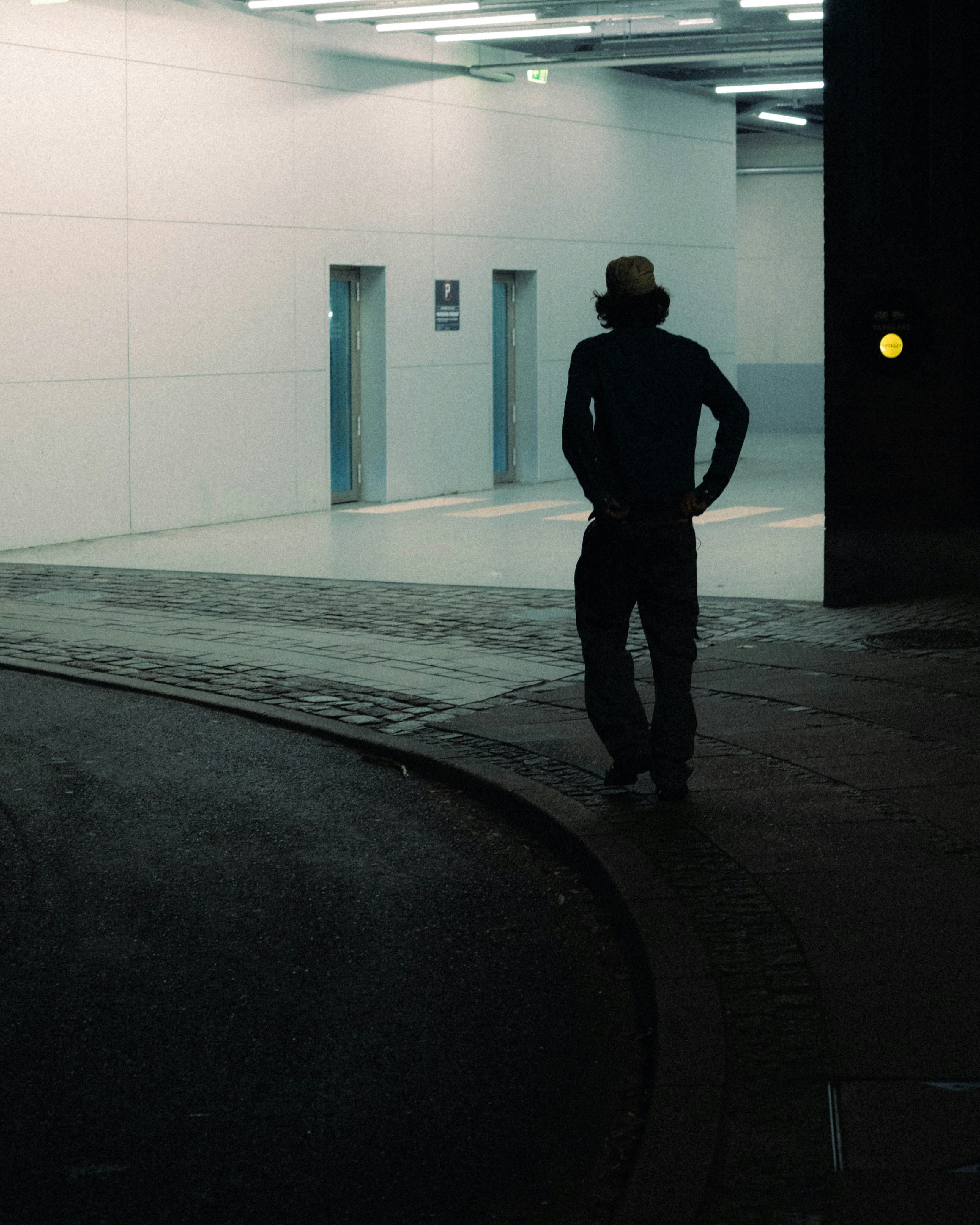 Man in hat stands in dimly lit modern hallway.