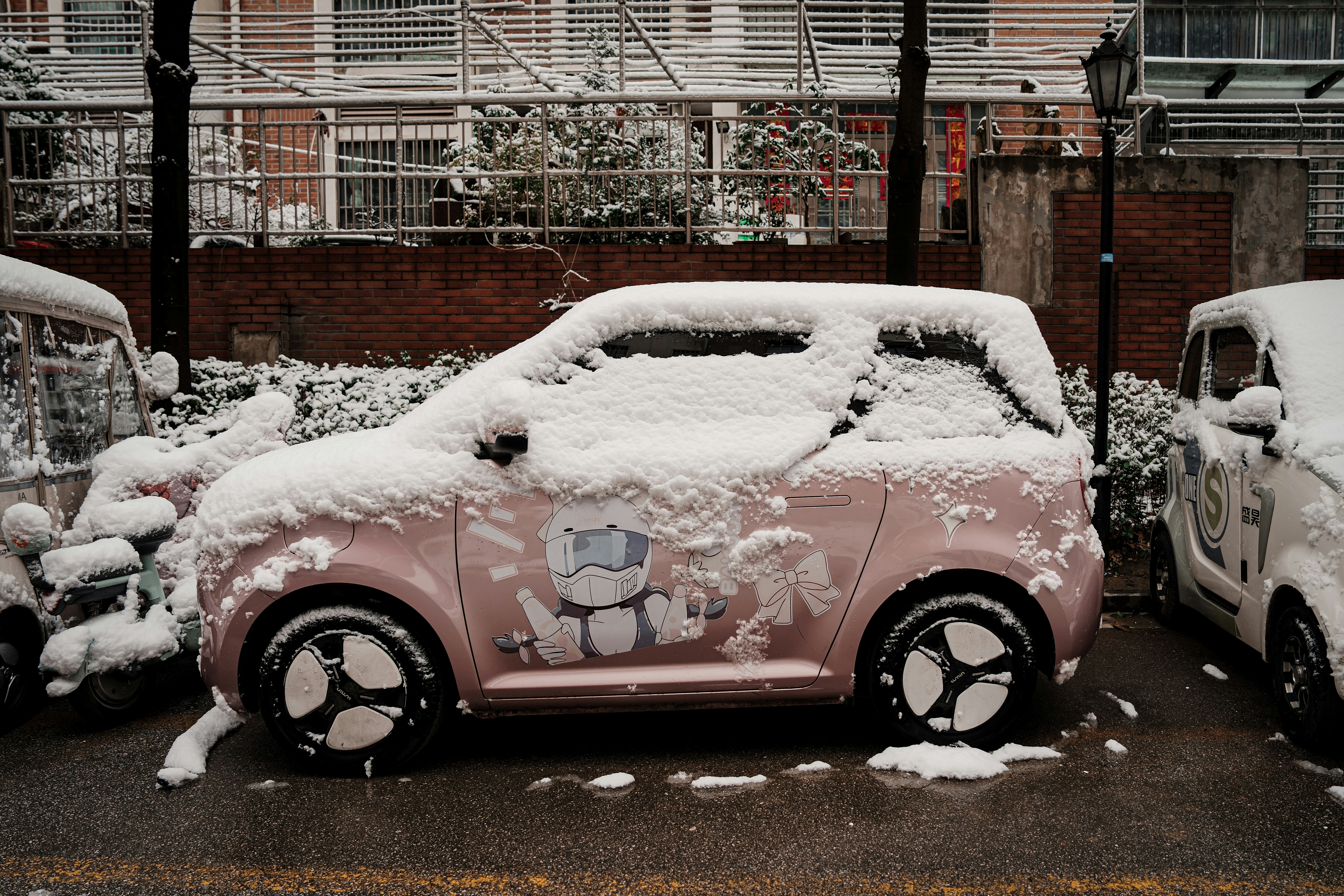 A pink car covered in snow on a street.