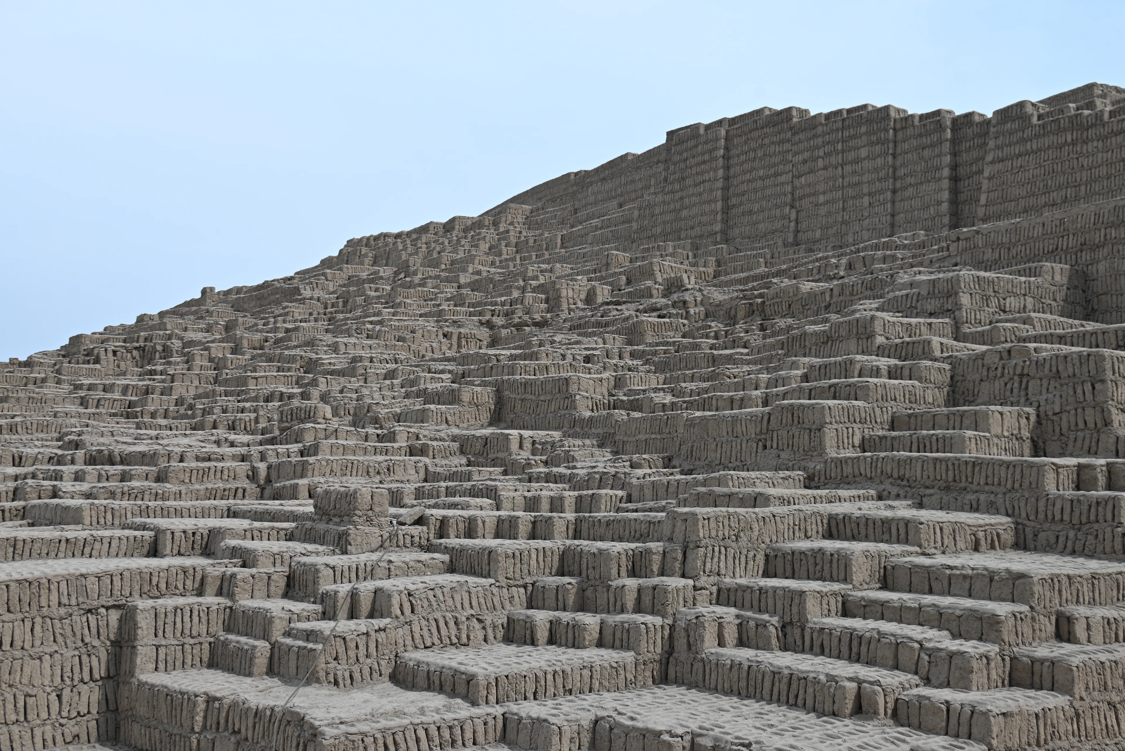 The adobe stepped pyramid of Huaca Pucllana in Lima, its thousands of hand-made mud bricks stacked on end like books in a bookshelf, sweeping diagonally up to a crenellated ridge against a clear blue sky