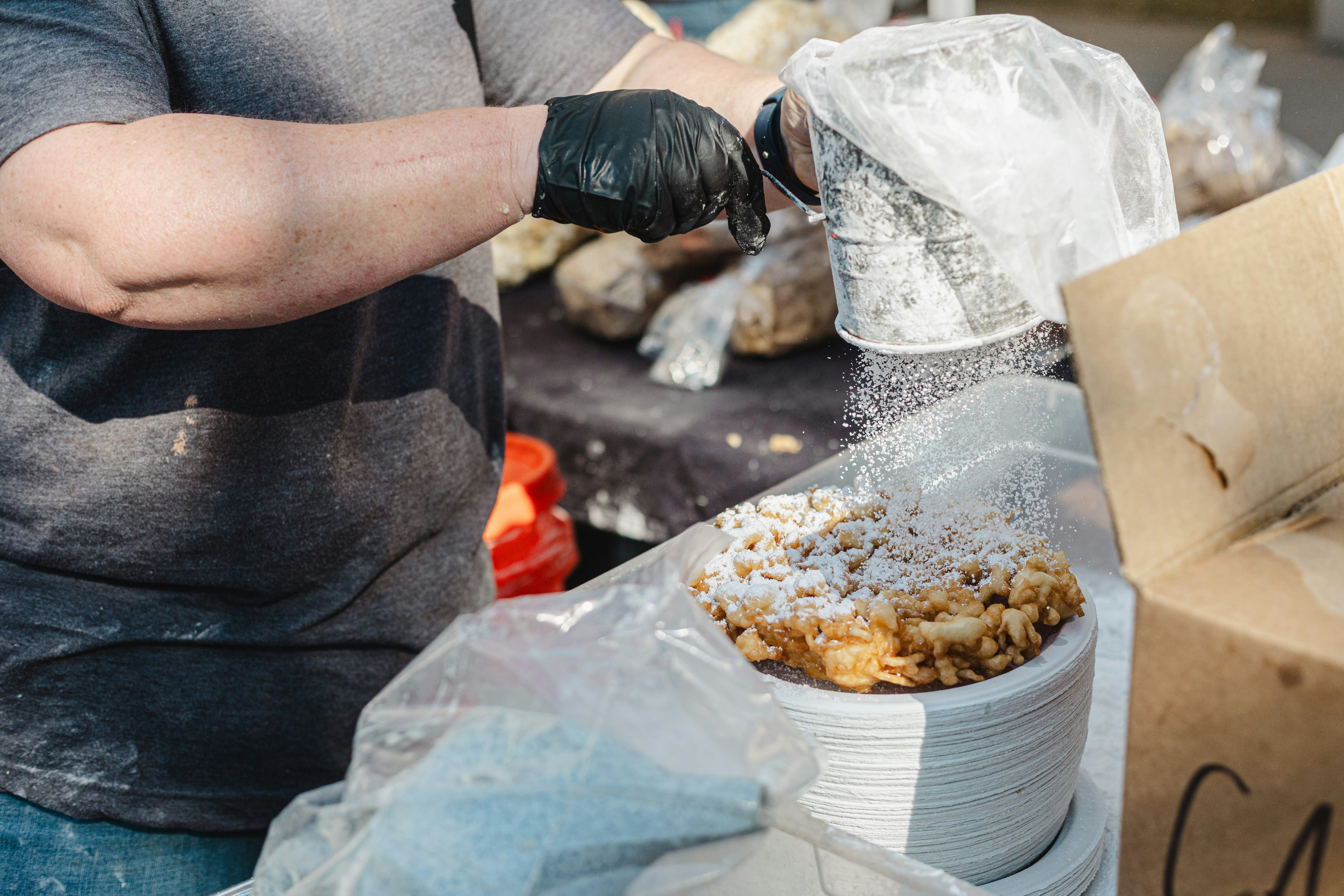 Baker dusting powdered sugar on funnel cake