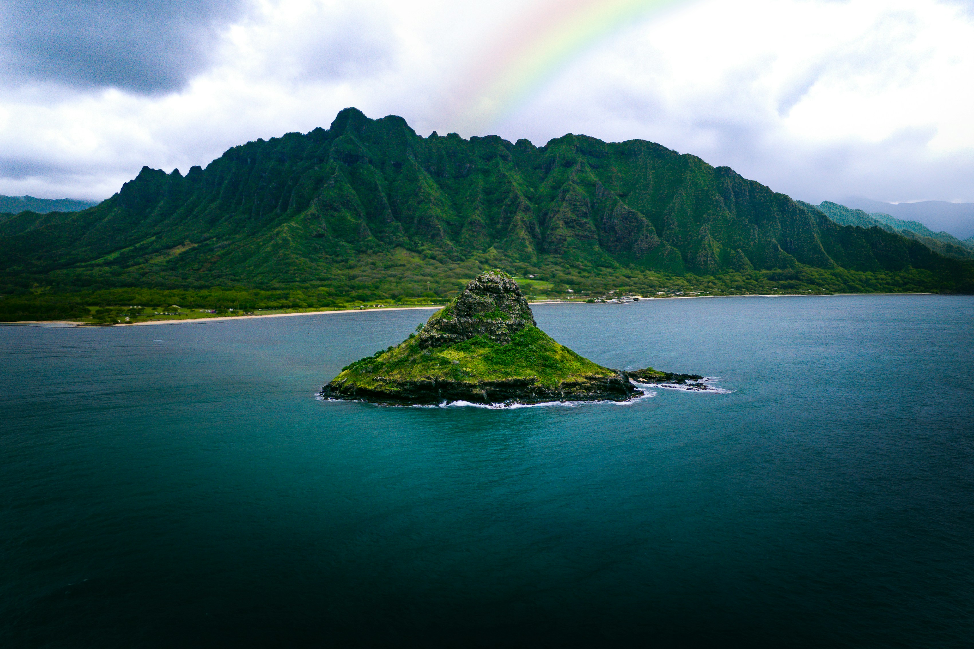 Île verte avec un arc-en-ciel au-dessus d’un océan calme.