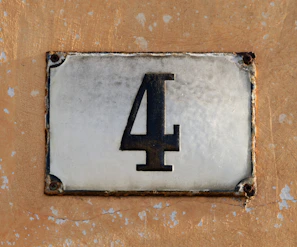 A weathered house number 4 on a textured wall.