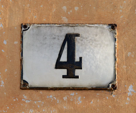 A weathered house number 4 on a textured wall