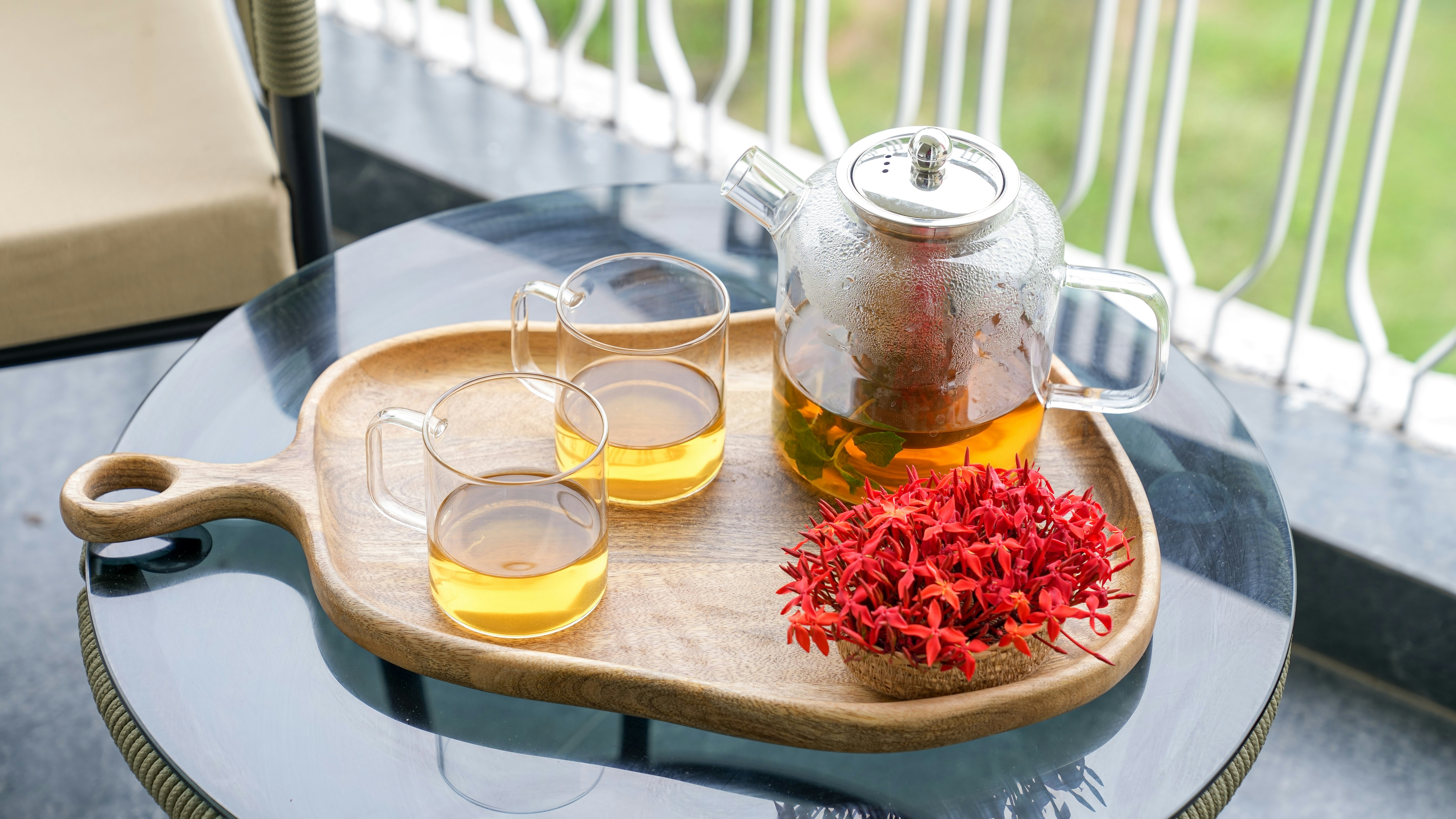 Tetera de cristal con té y tazas sobre una bandeja de madera