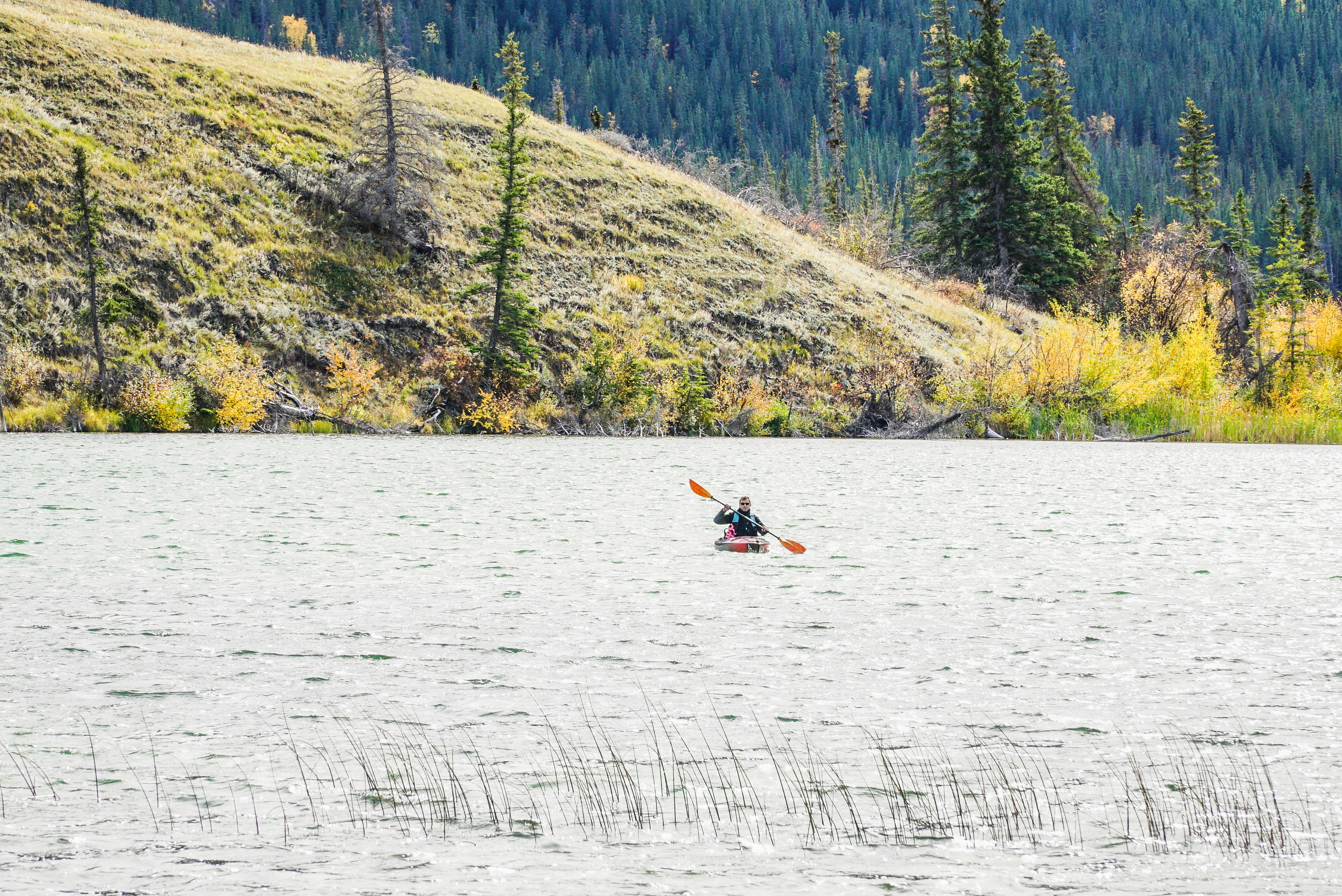 A person kayaks on a calm, rippling lake.