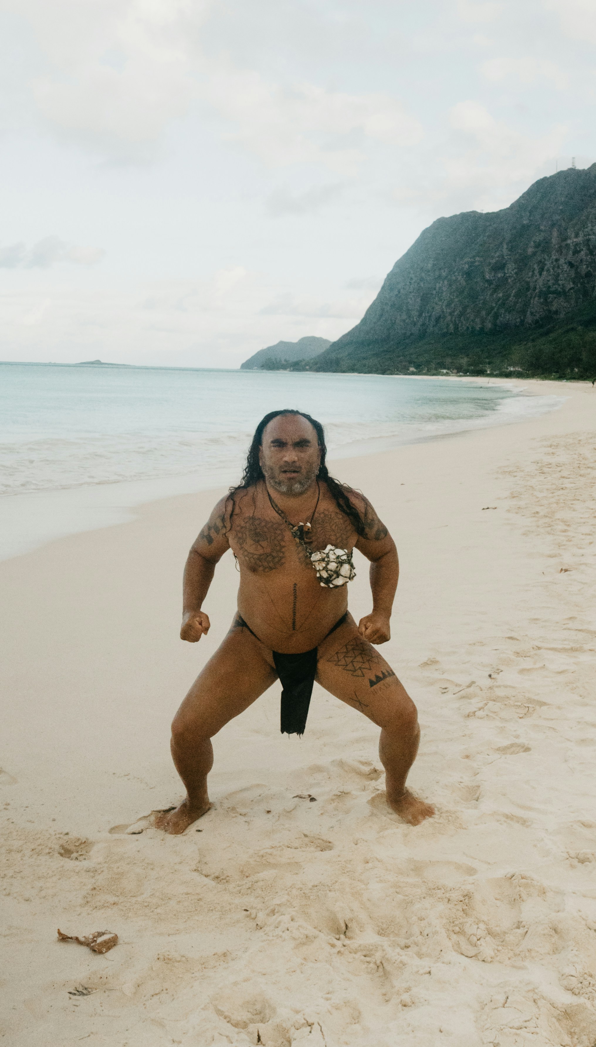 Man in traditional attire on a sandy beach.