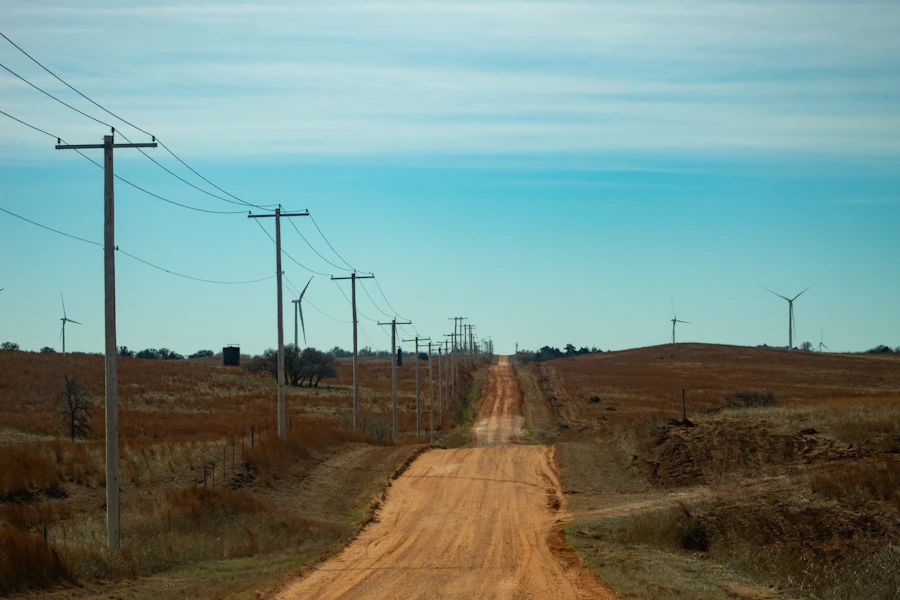 A red dirt road between power poles toward wind turbines