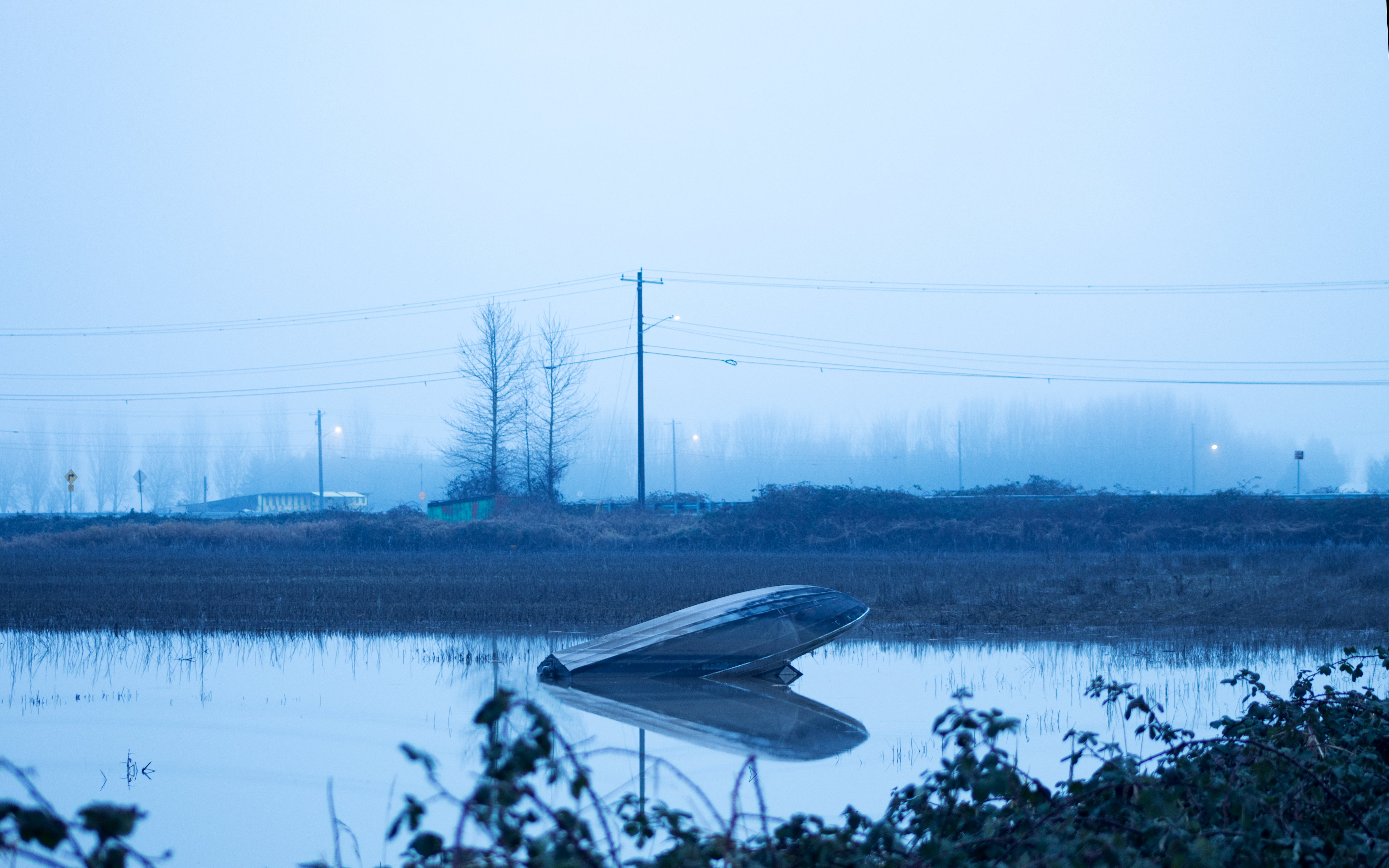 Bateau renversé immergé dans une eau peu profonde sous un ciel brumeux.
