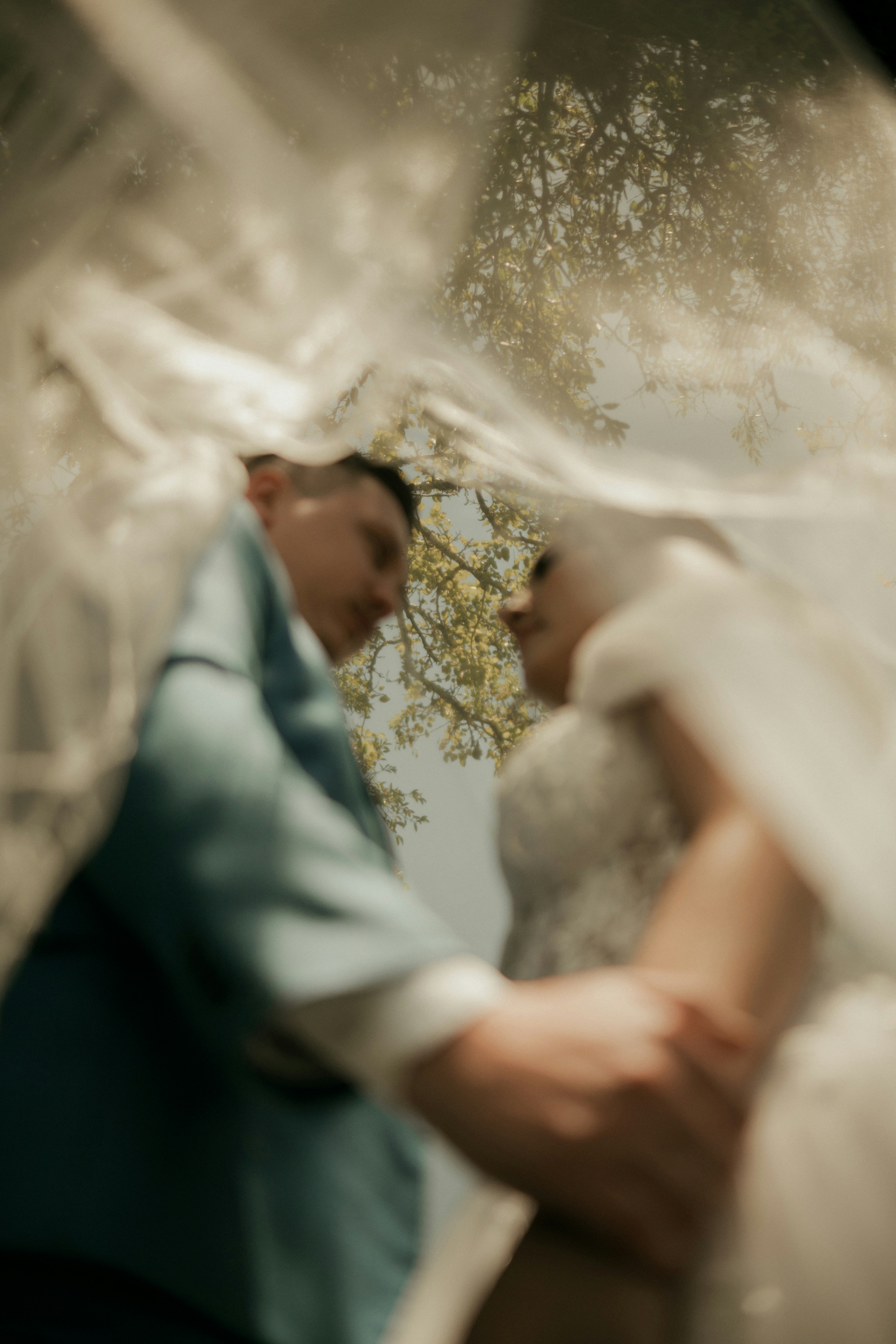 Bride and groom under a veil with trees