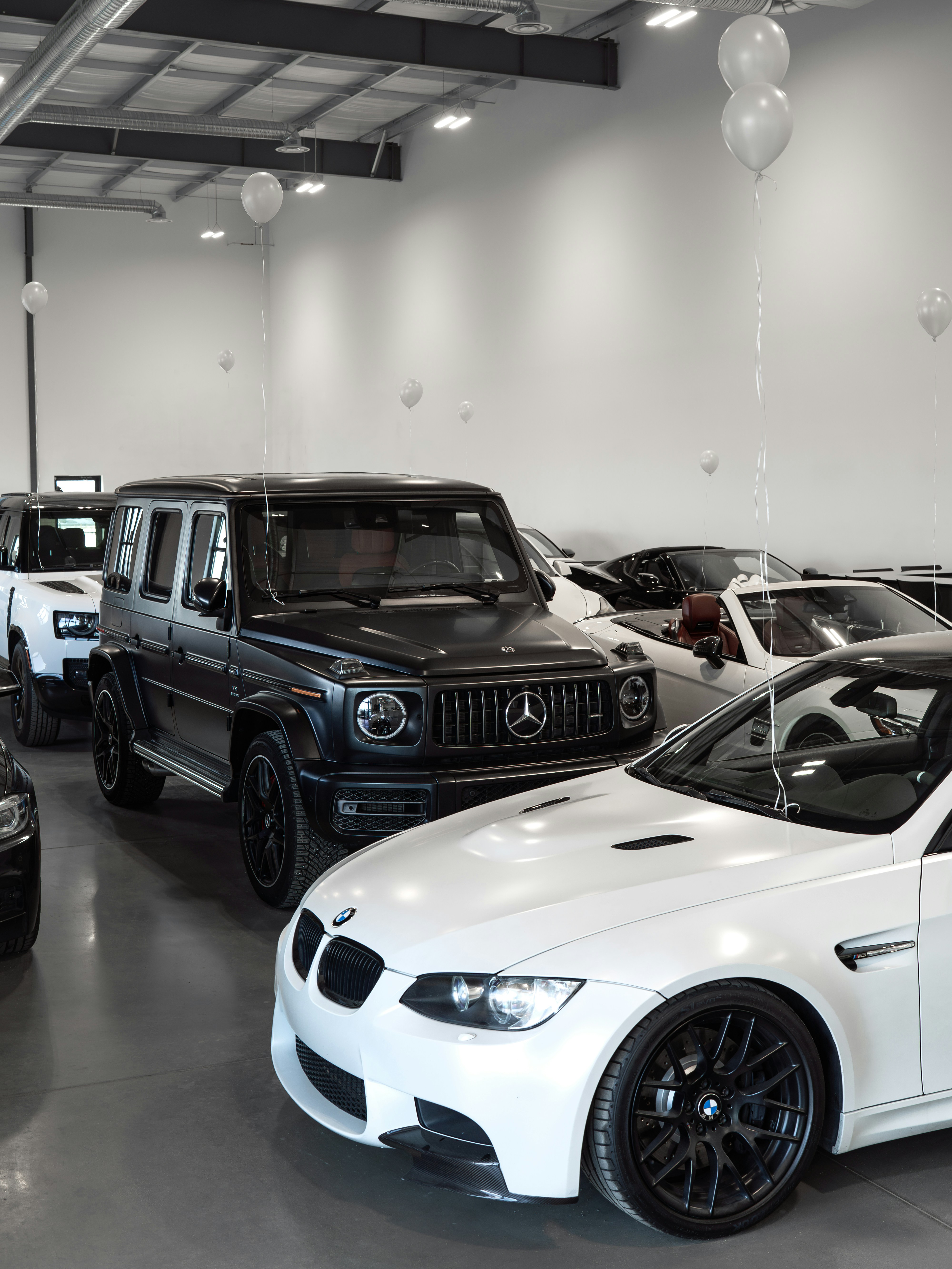 Luxury cars displayed in a showroom with balloons.