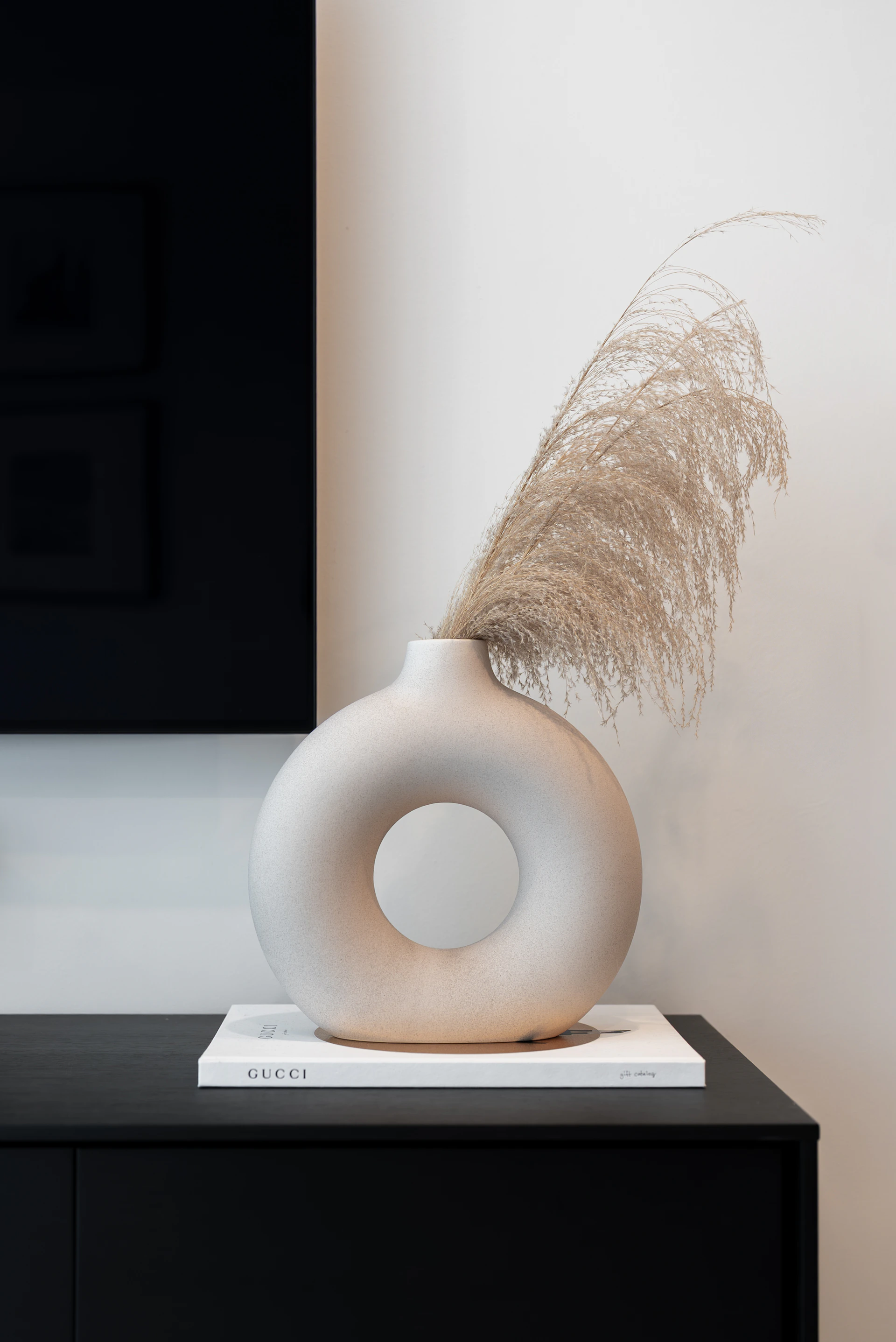 A modern donut-shaped vase with dried grass