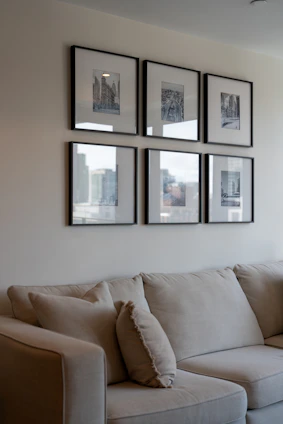 Six framed artworks hang above a light-colored sofa.