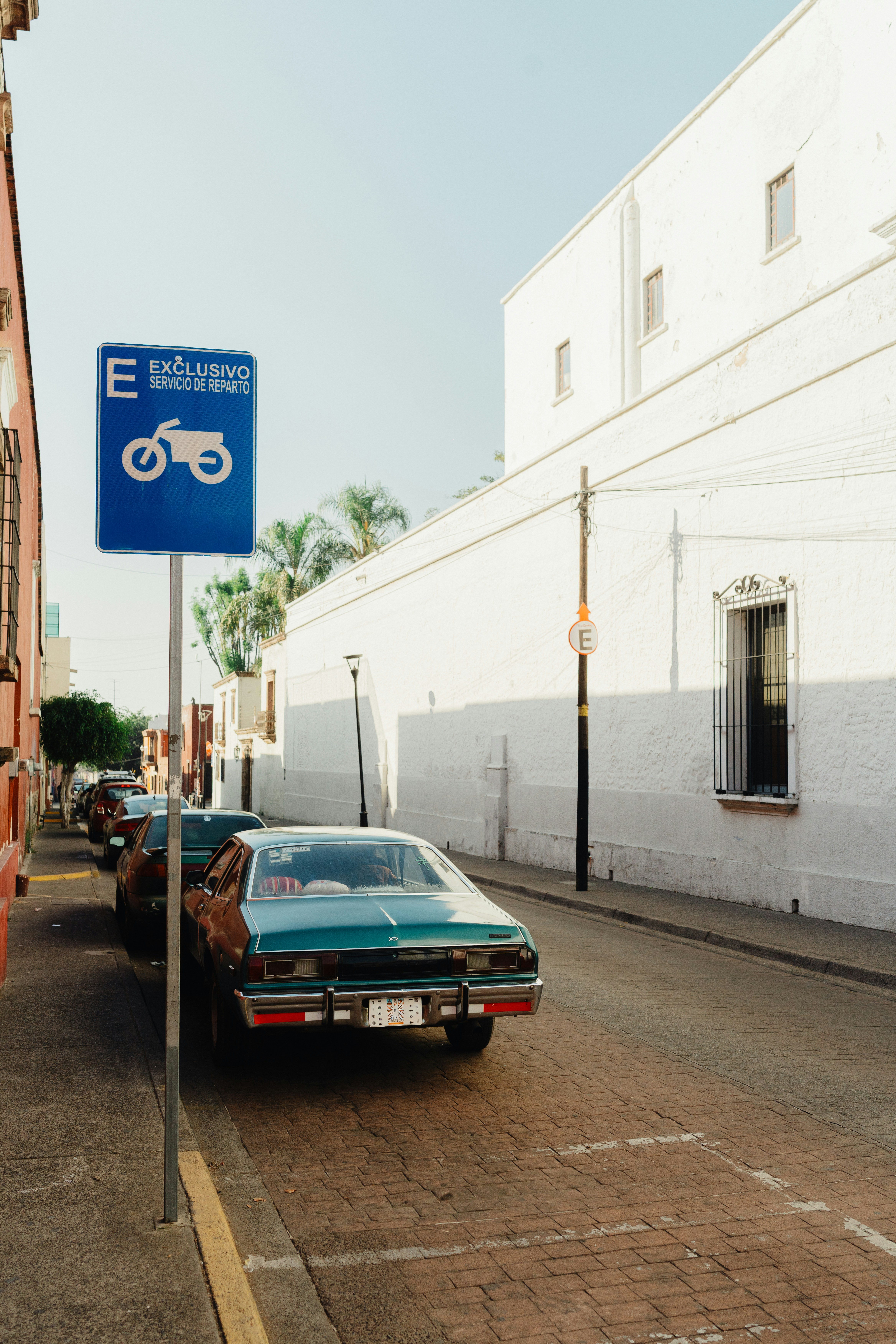 Cars parked on a cobblestone street with white building.