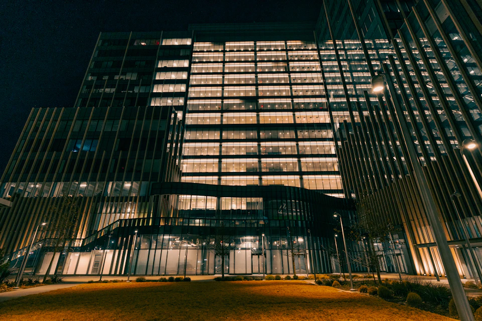 Large modern glass and steel skyscraper dominates street corner with surrounding cityscape at dusk