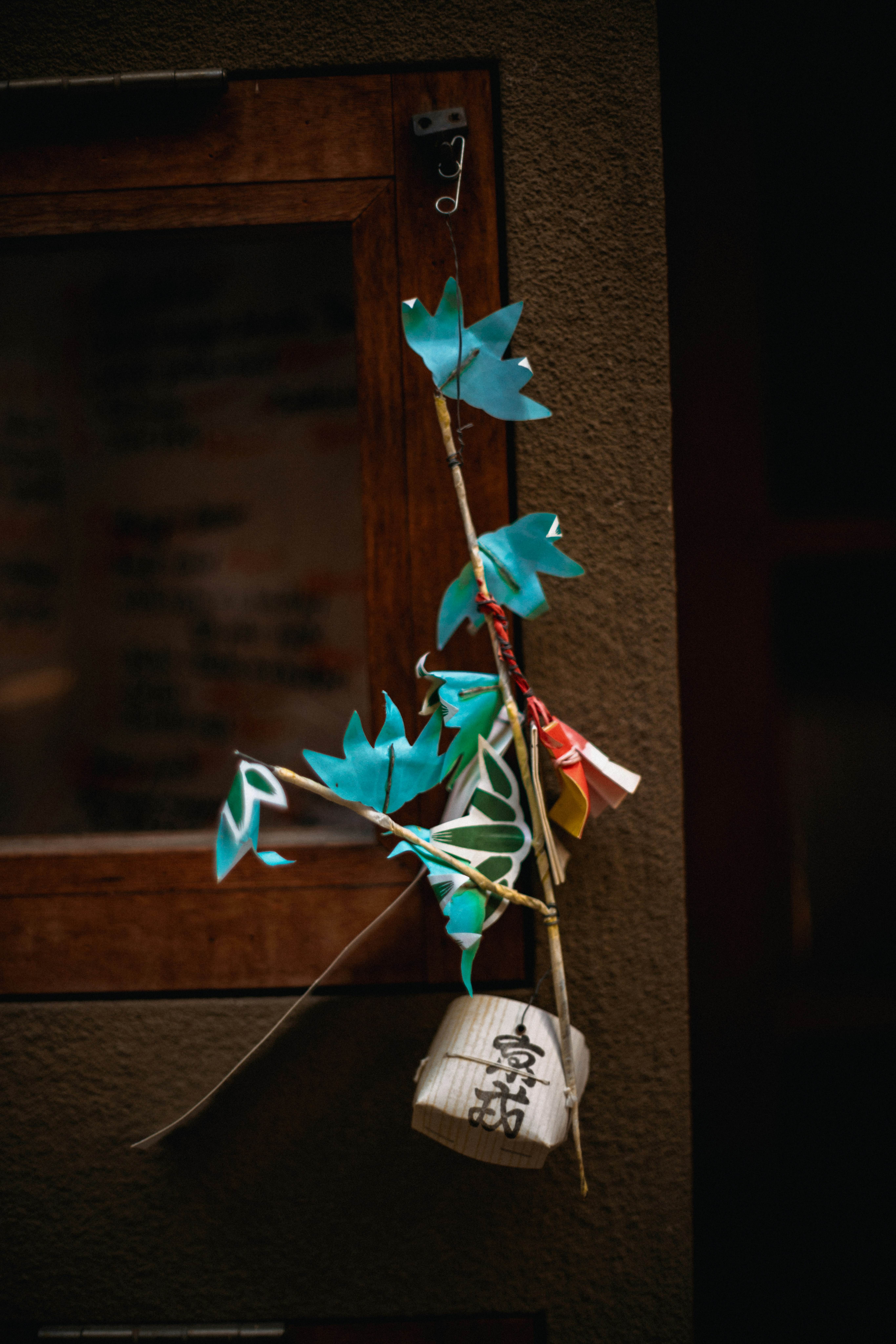 Blue origami flowers and charms hang on a wooden frame.