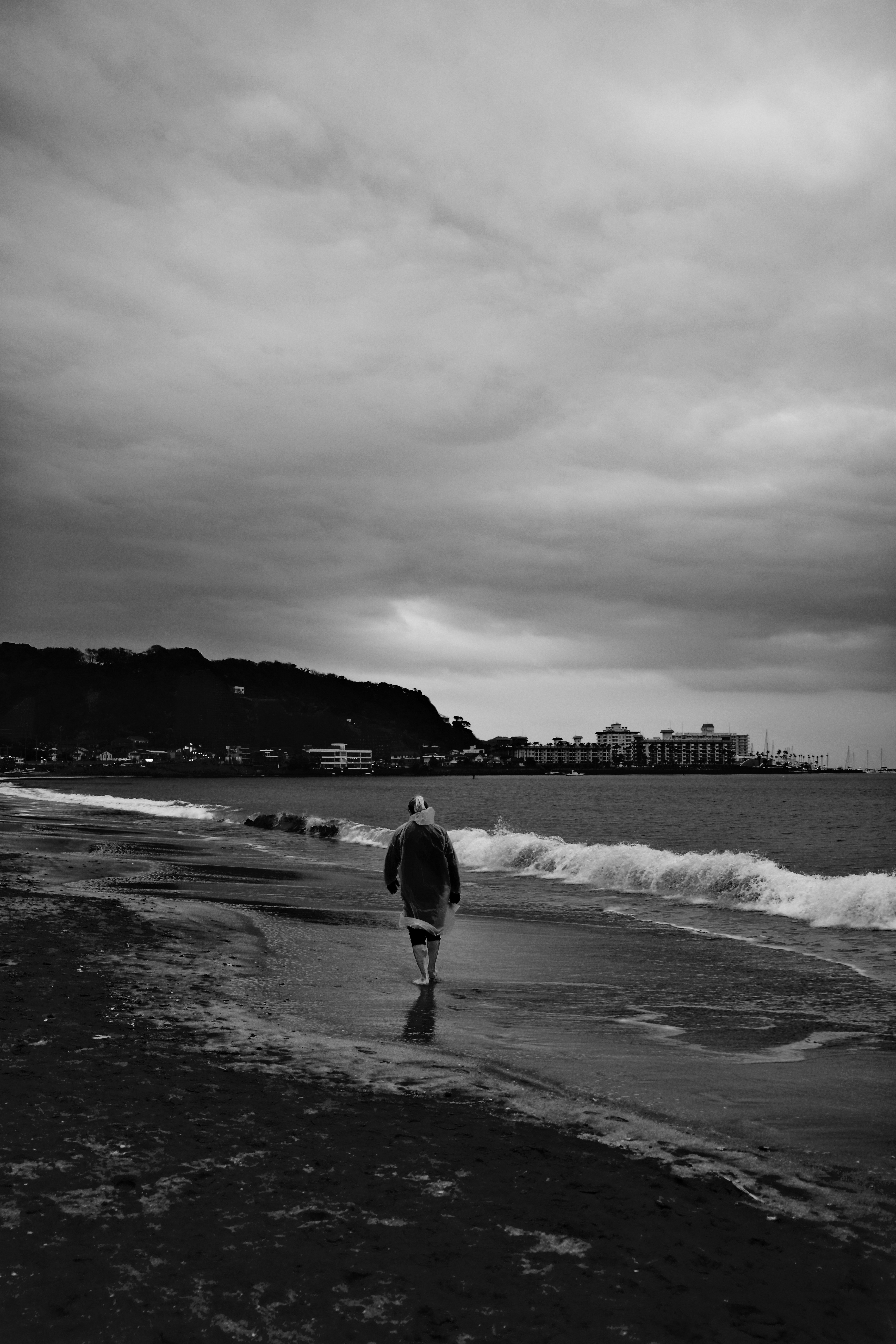 Person walks on a beach with stormy clouds.