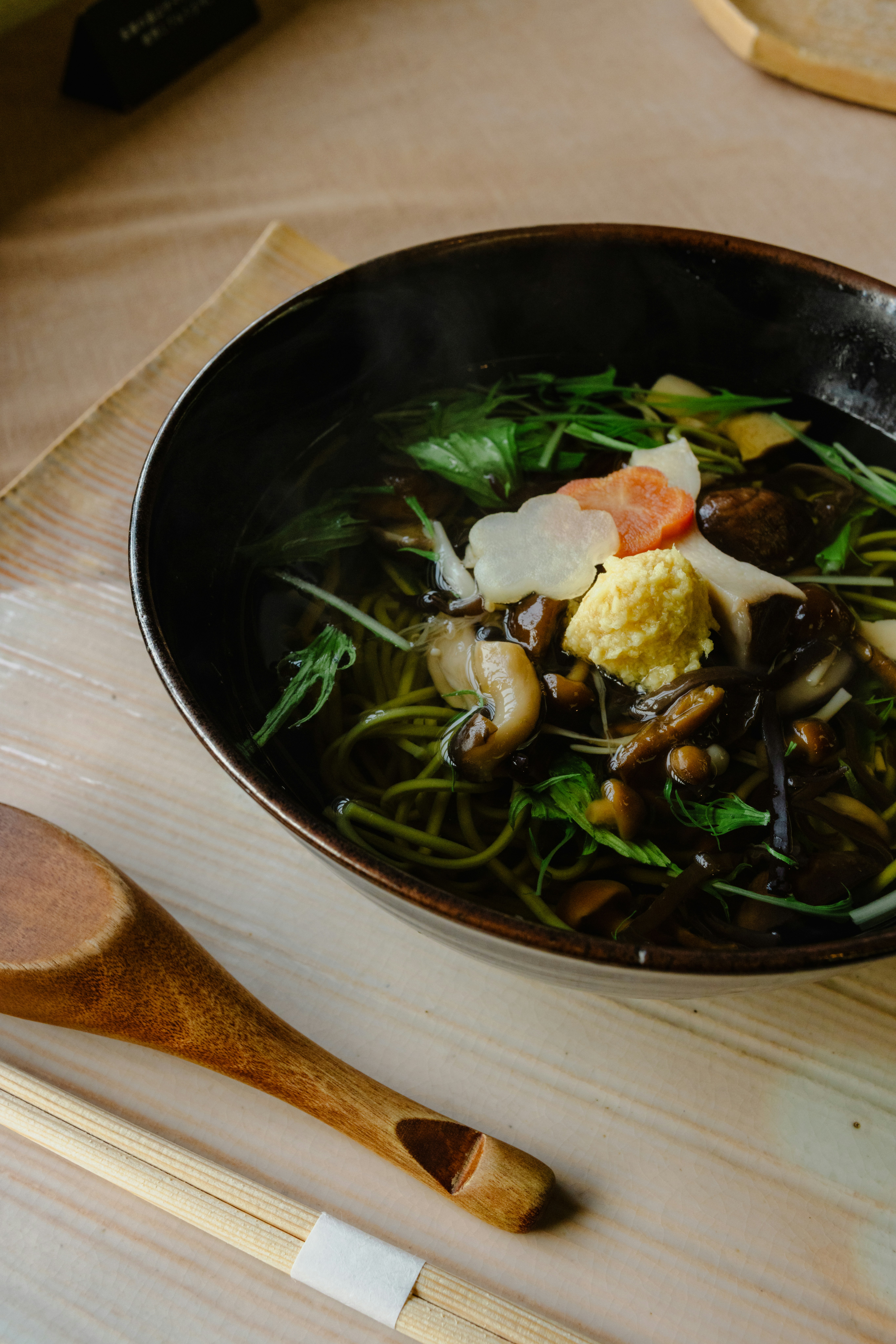 A steaming bowl of soba noodles with mushrooms and vegetables.