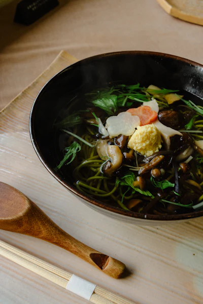 A steaming bowl of soba noodles with mushrooms and vegetables