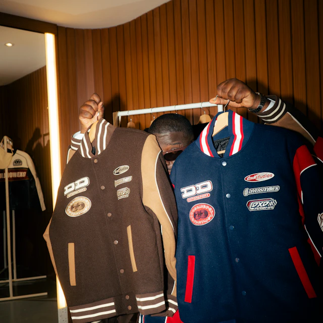 A man holding up two varsity jackets, one brown and one blue