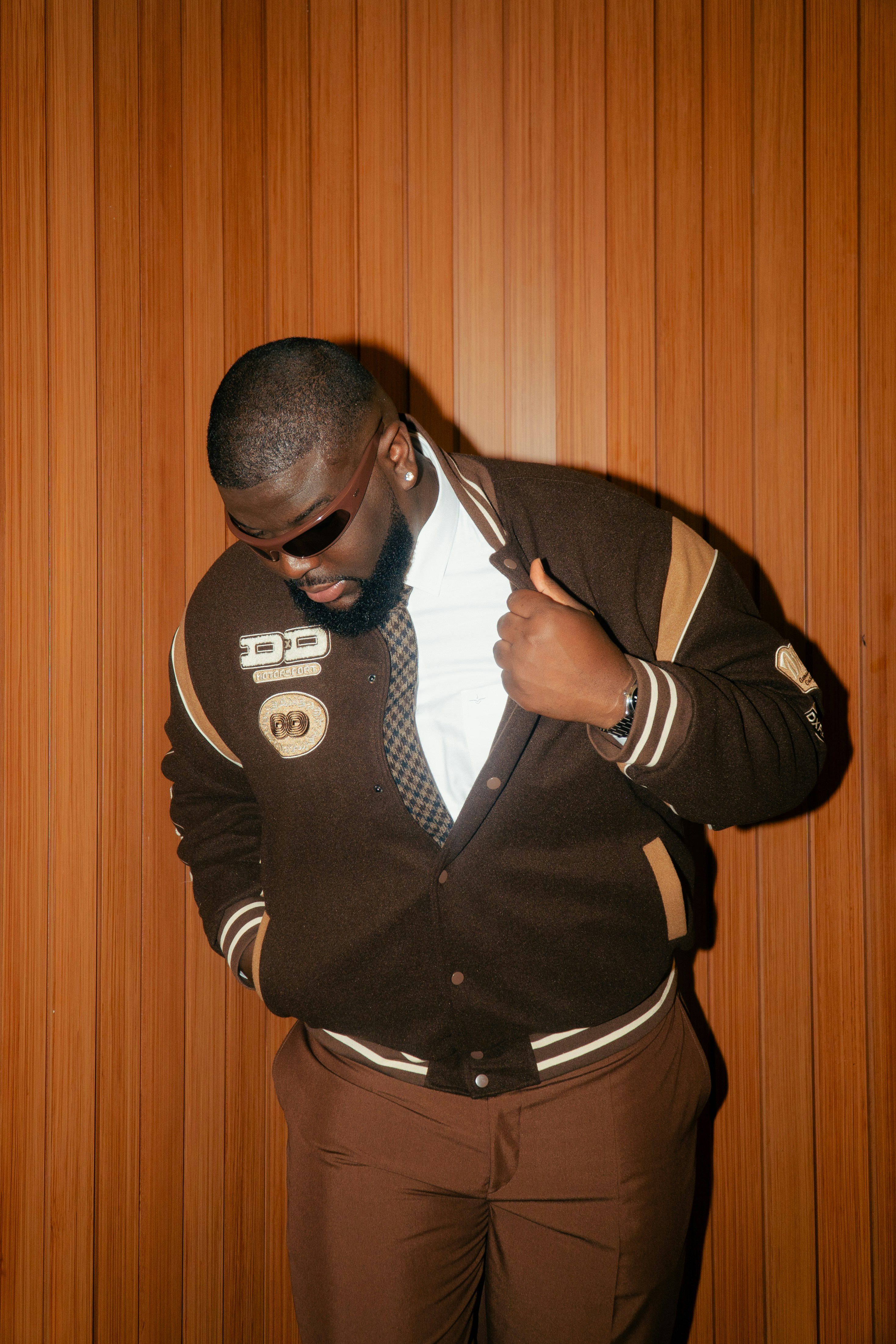 Uomo con una giacca marrone varsity e occhiali da sole