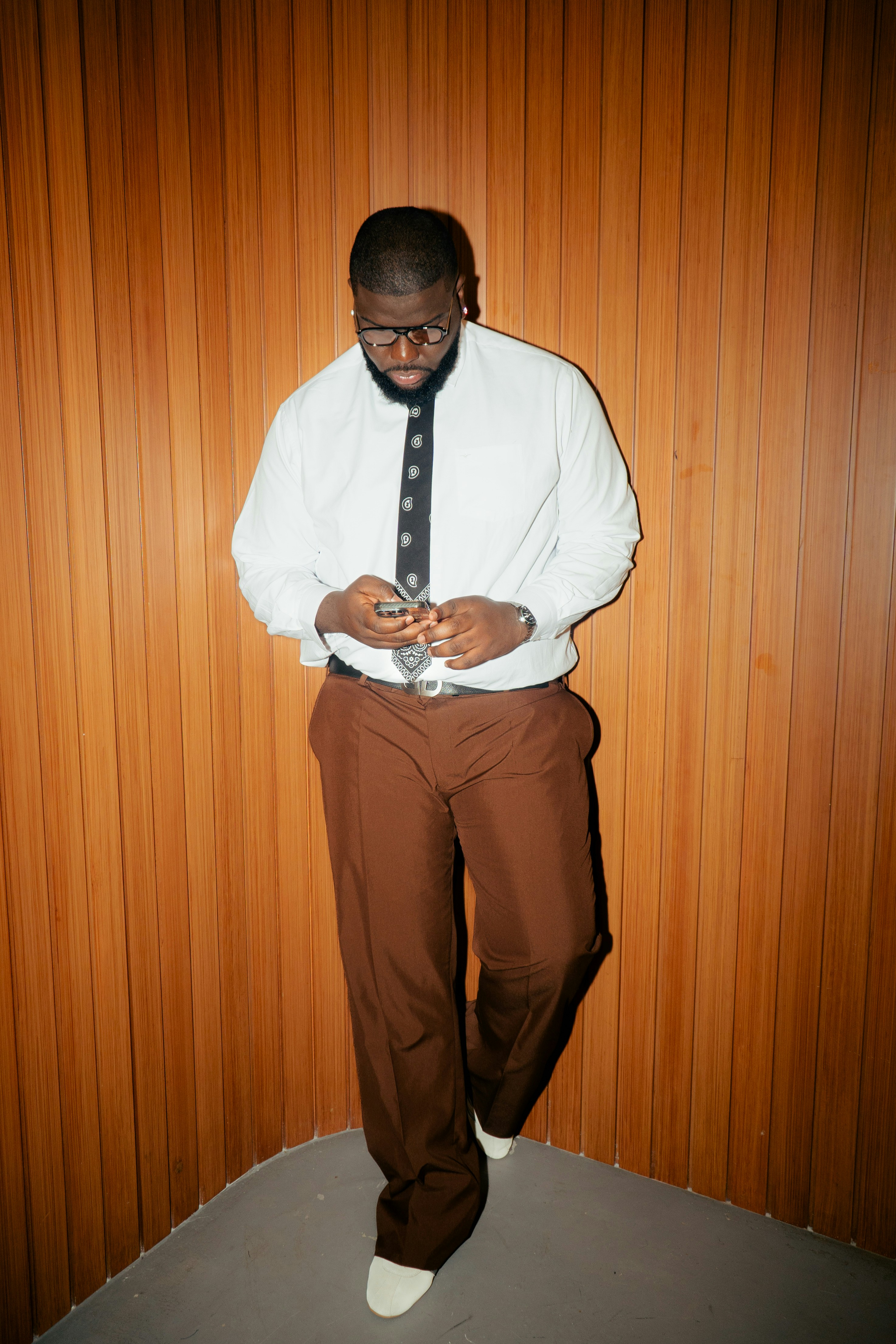 Man in white shirt and brown pants looking at phone.