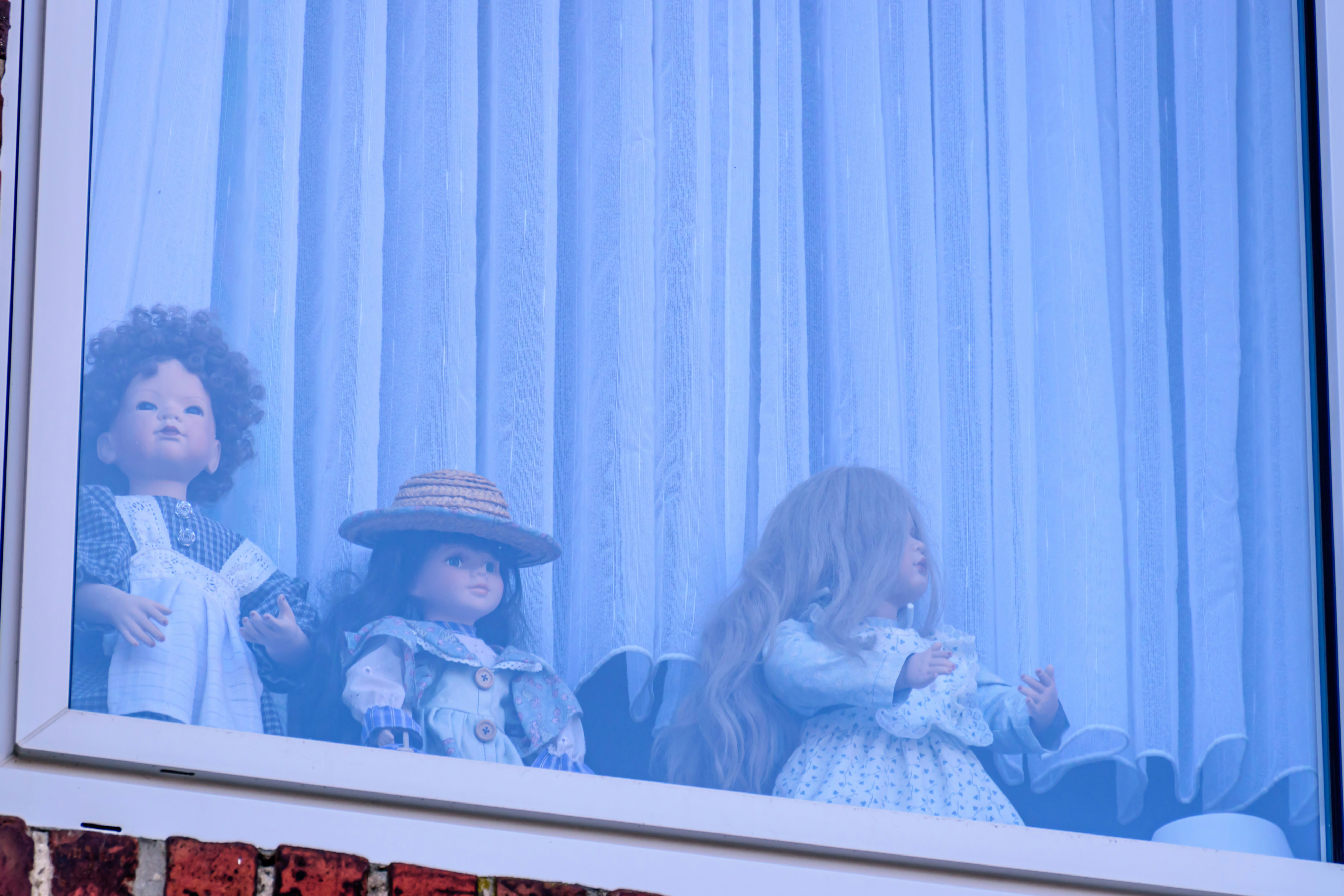Dolls are looking out a window behind curtains