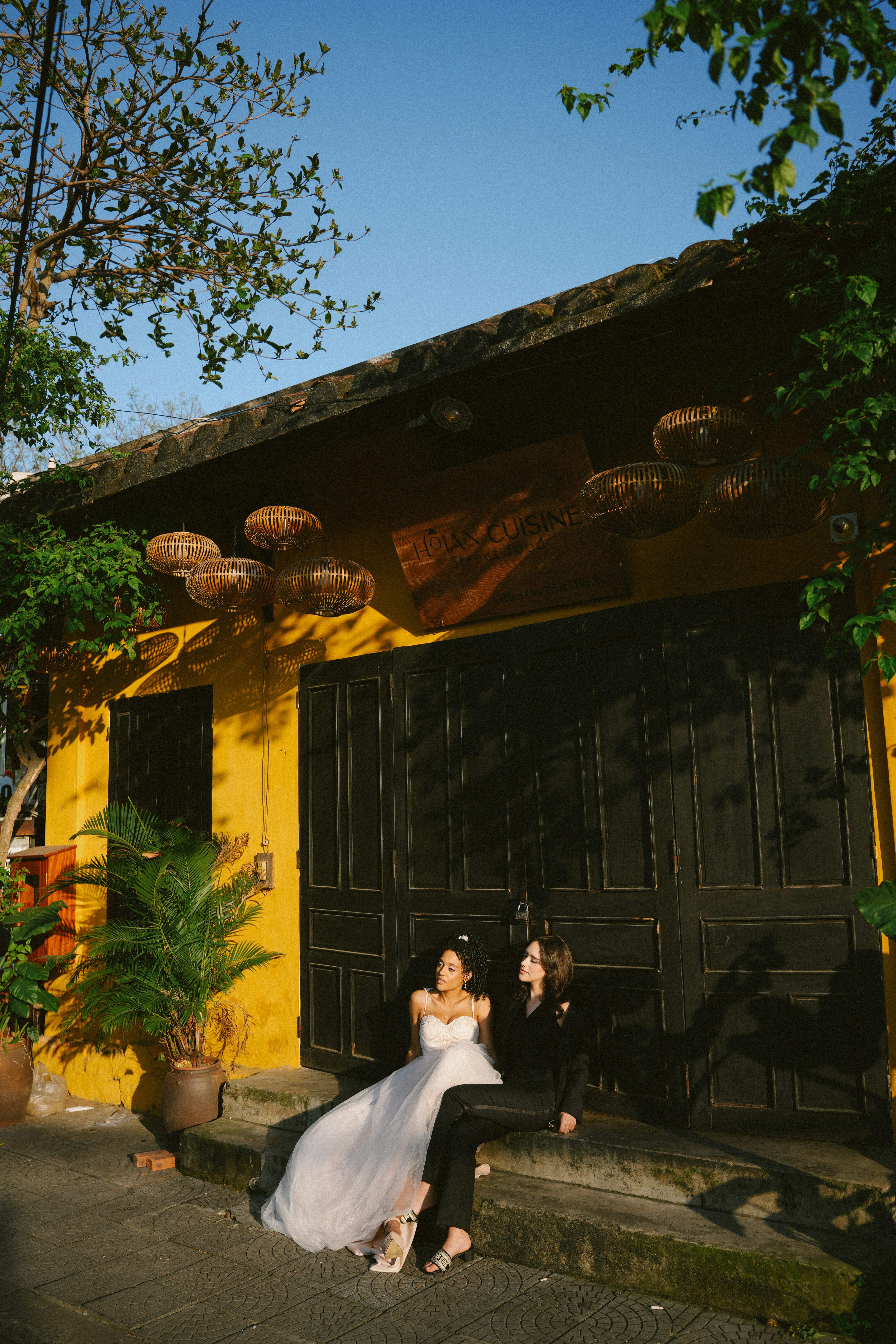 Due donne in abiti formali sedute fuori da un edificio giallo.