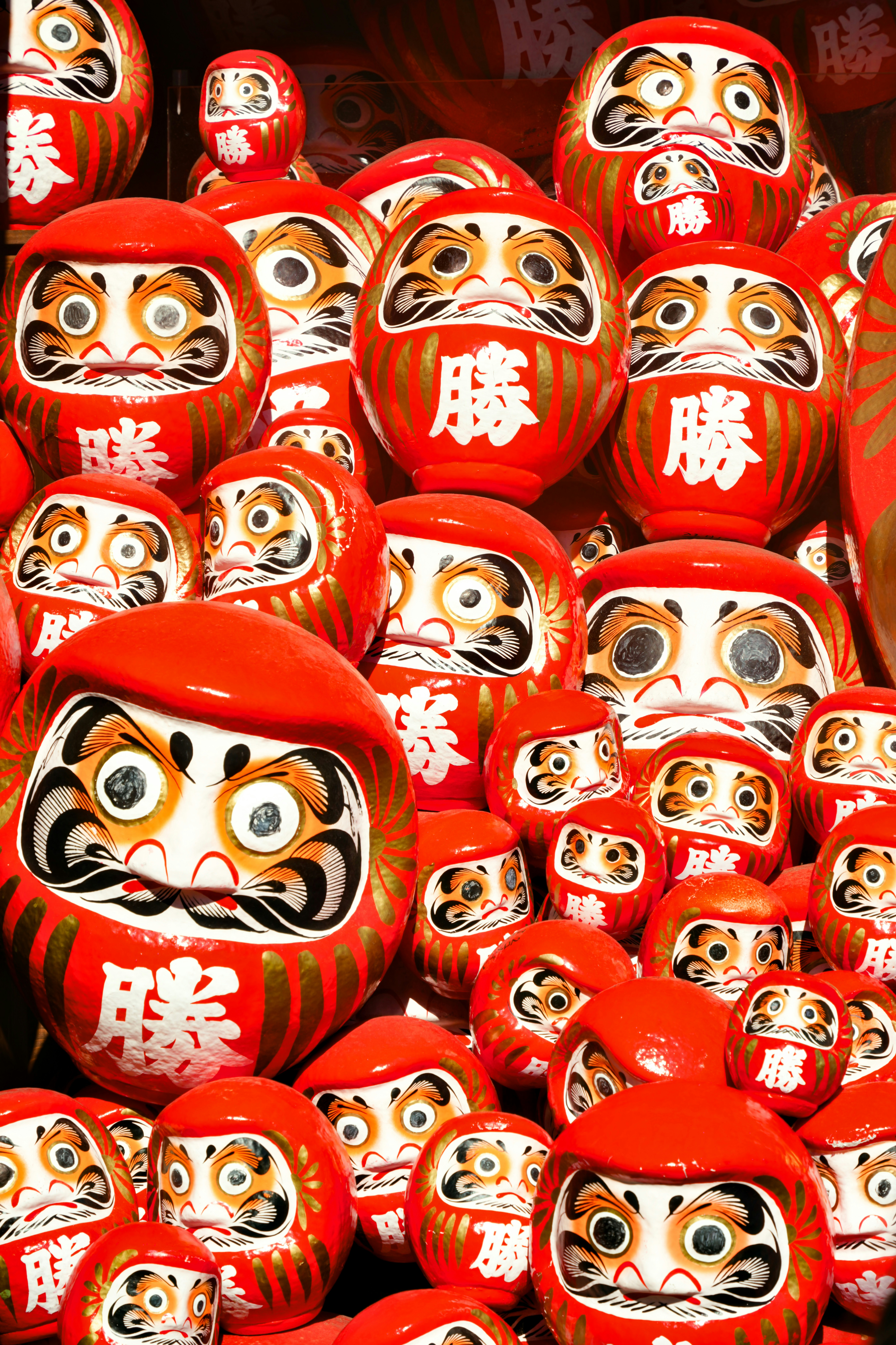 A collection of red daruma dolls with gold accents.