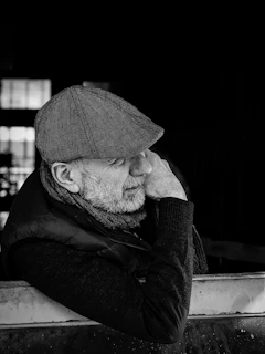 Elderly man in flat cap and scarf looking away thoughtfully