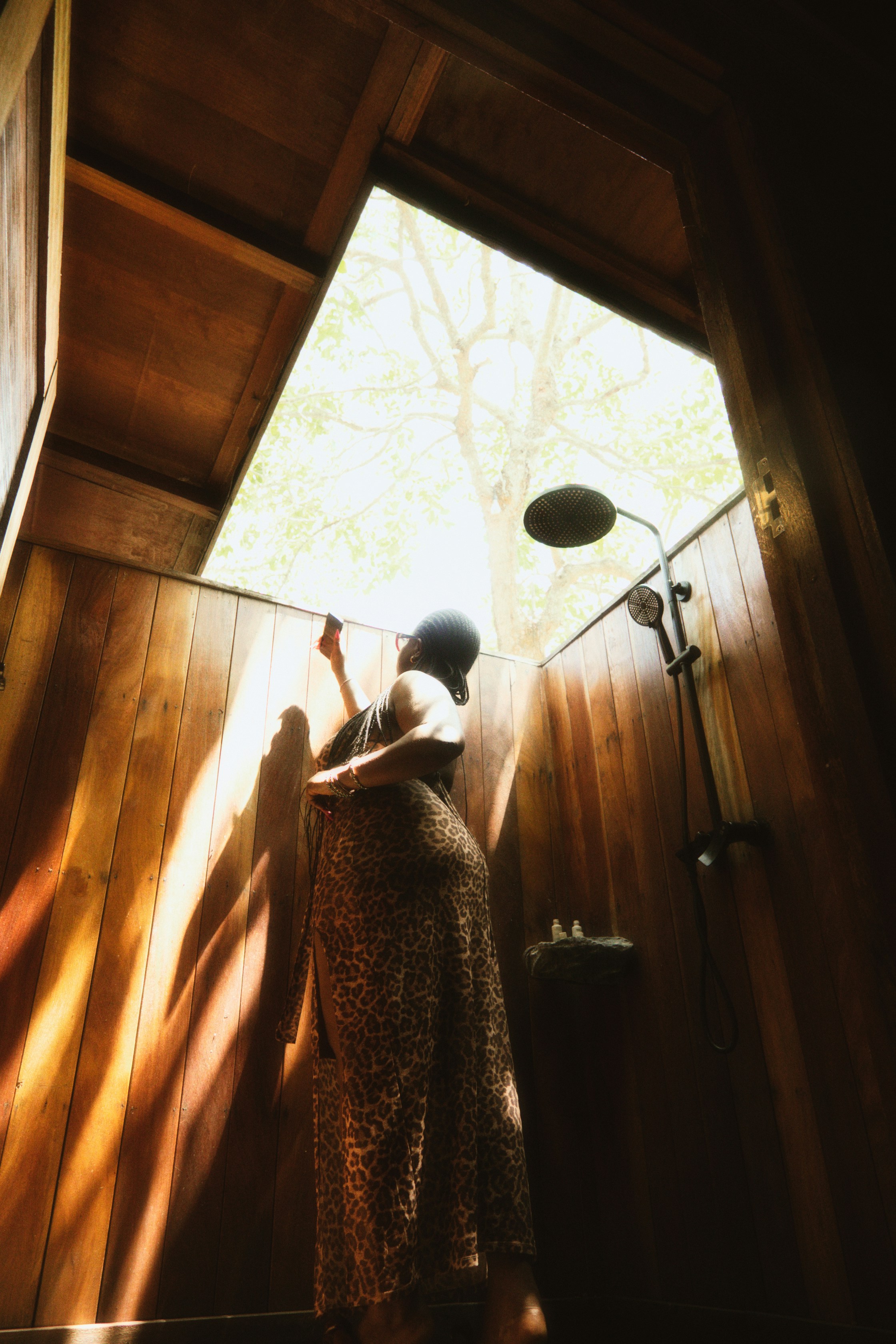 Woman in leopard print dress in rustic outdoor shower.