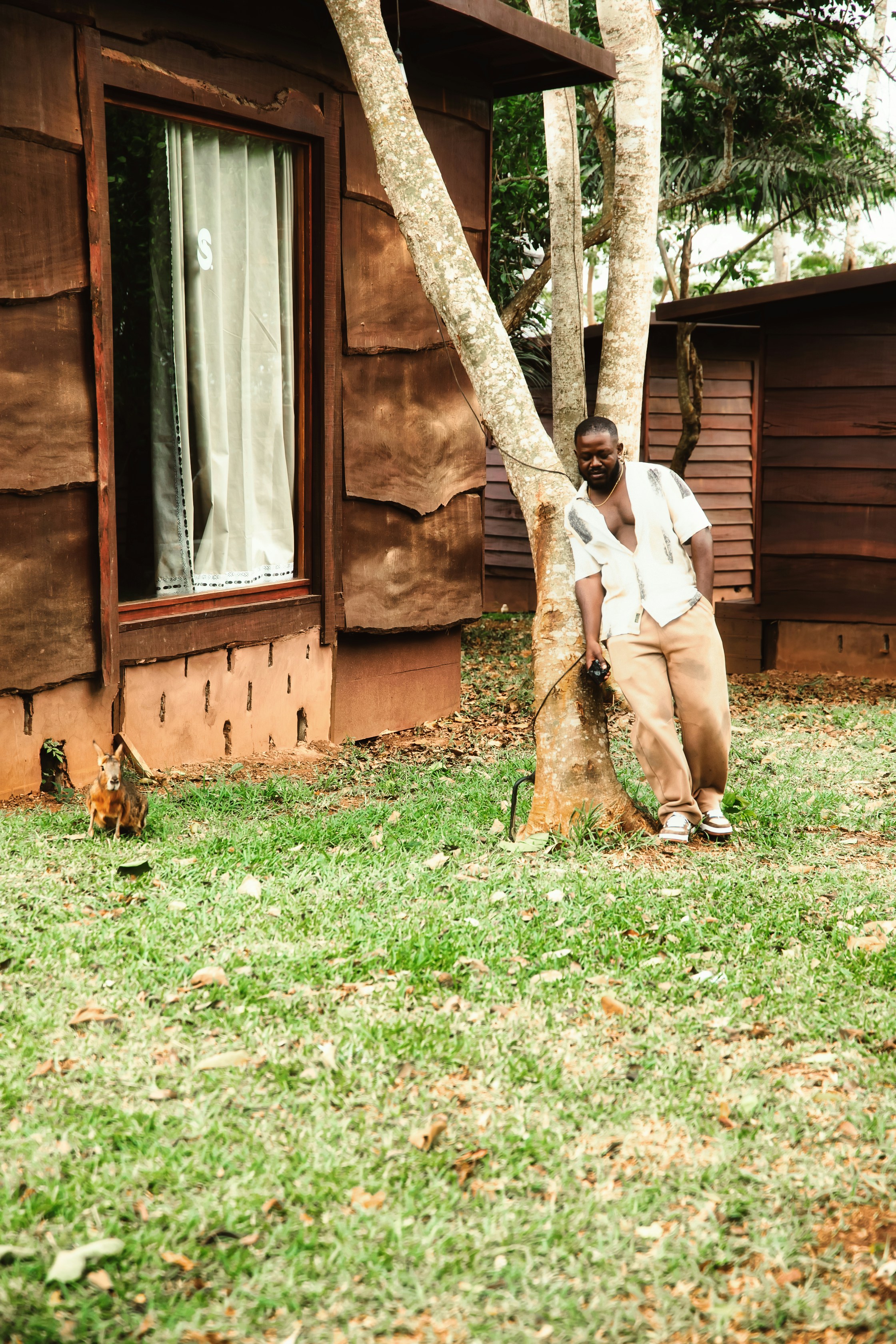 Man leaning against a tree near wooden cabins.