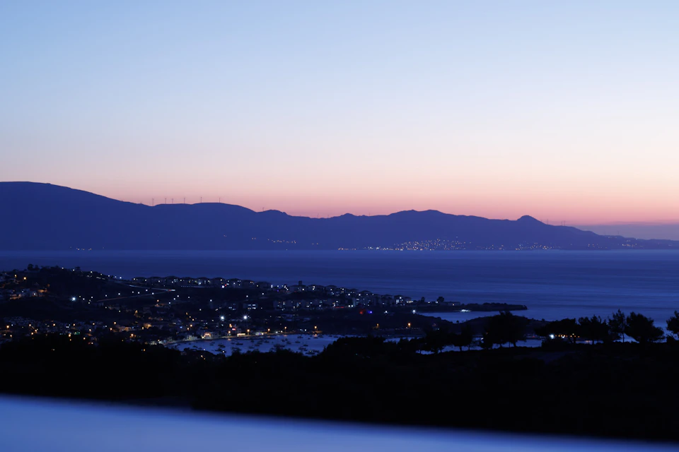 Sunset over mountains with ocean and buildings in a serene coastal landscape at dusk