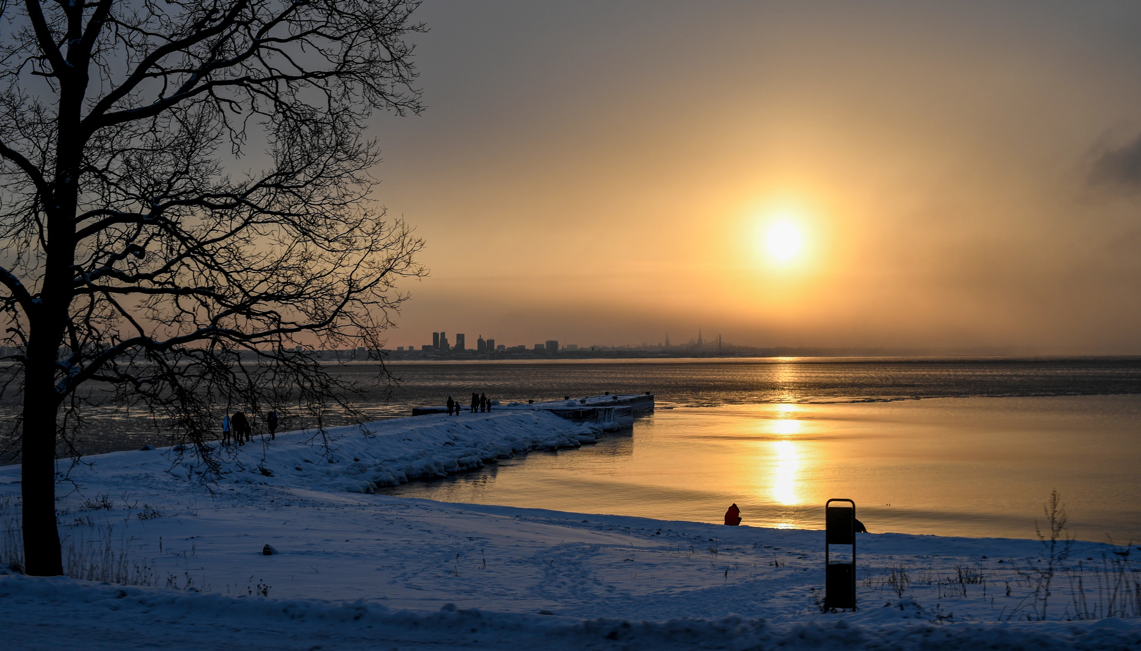 Winter sunset at a pier with snow and silhouetted walkers