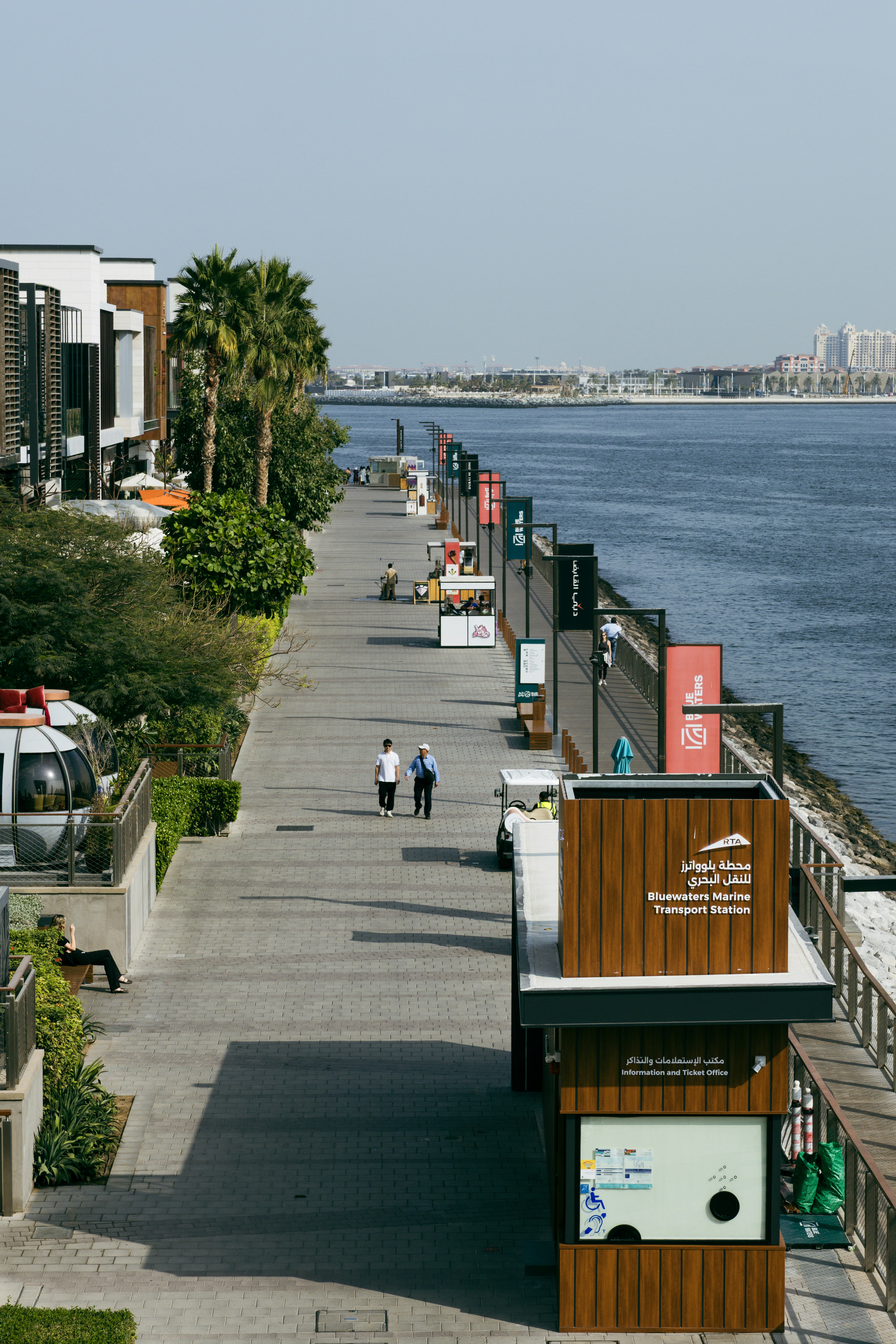 人々は現代的な建物のあるウォーターフロントの遊歩道を歩いています。