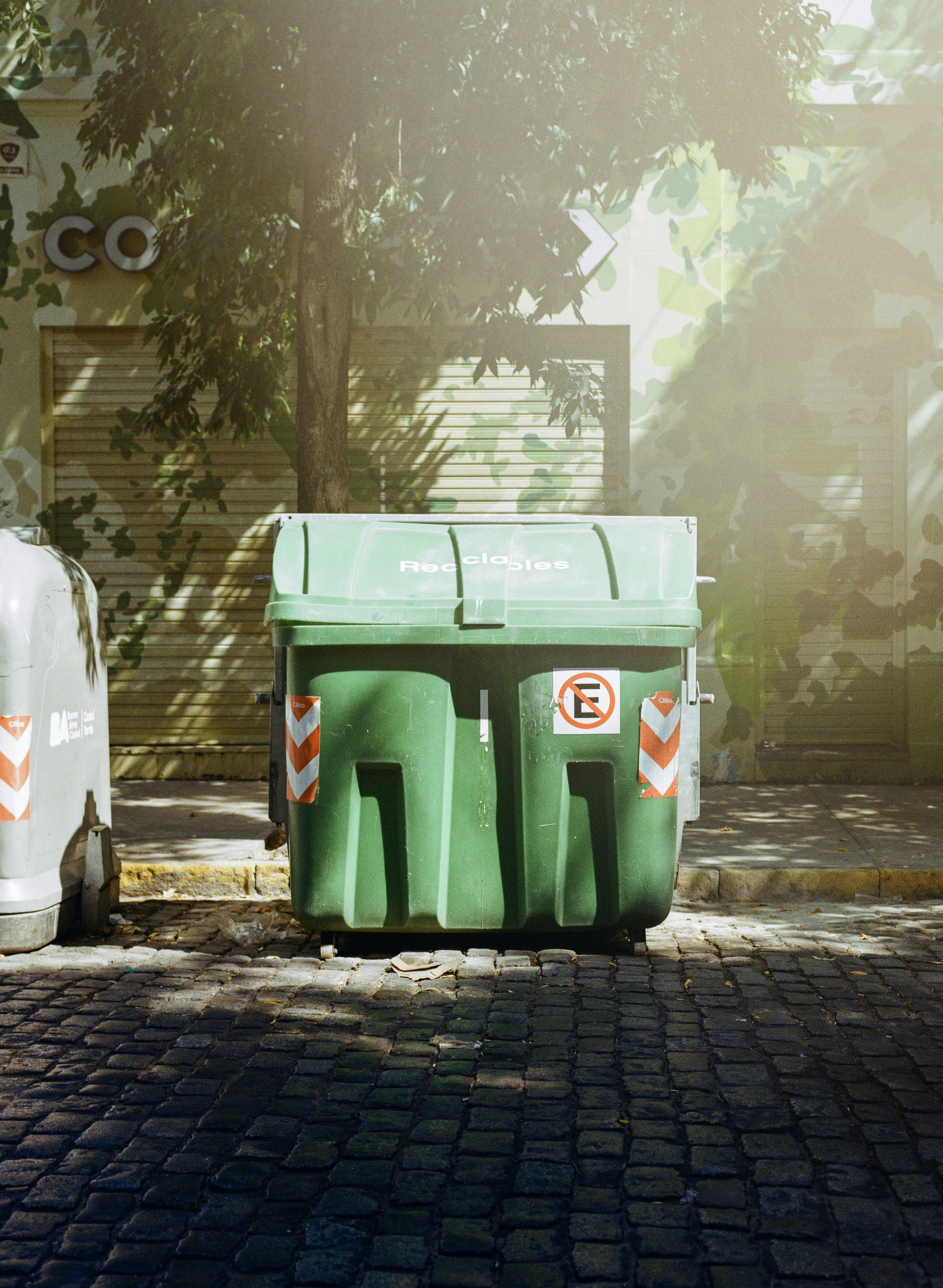 Dois grandes contêineres verdes em uma rua de paralelepípedos
