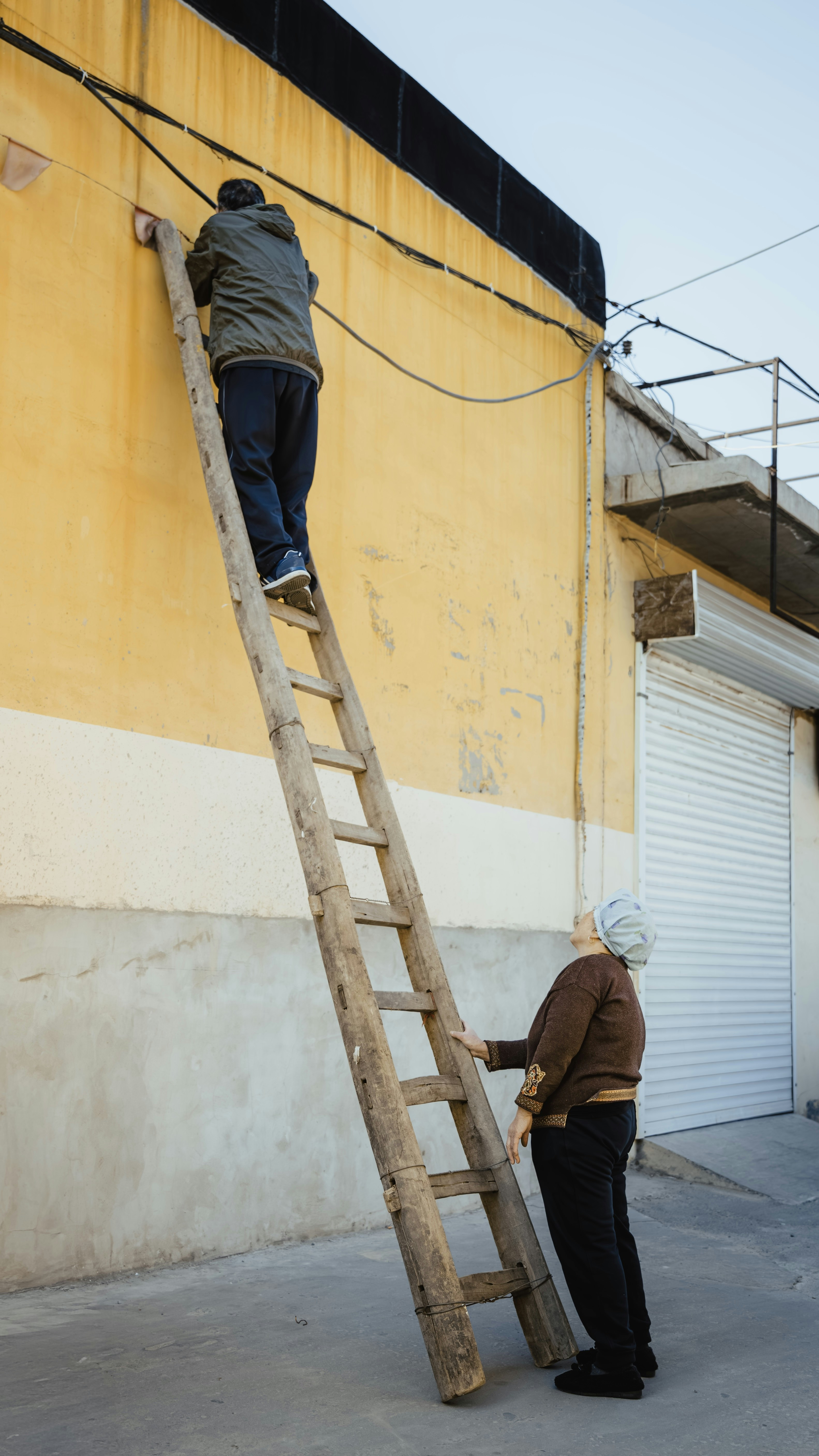 Man climbs ladder, woman watches below.