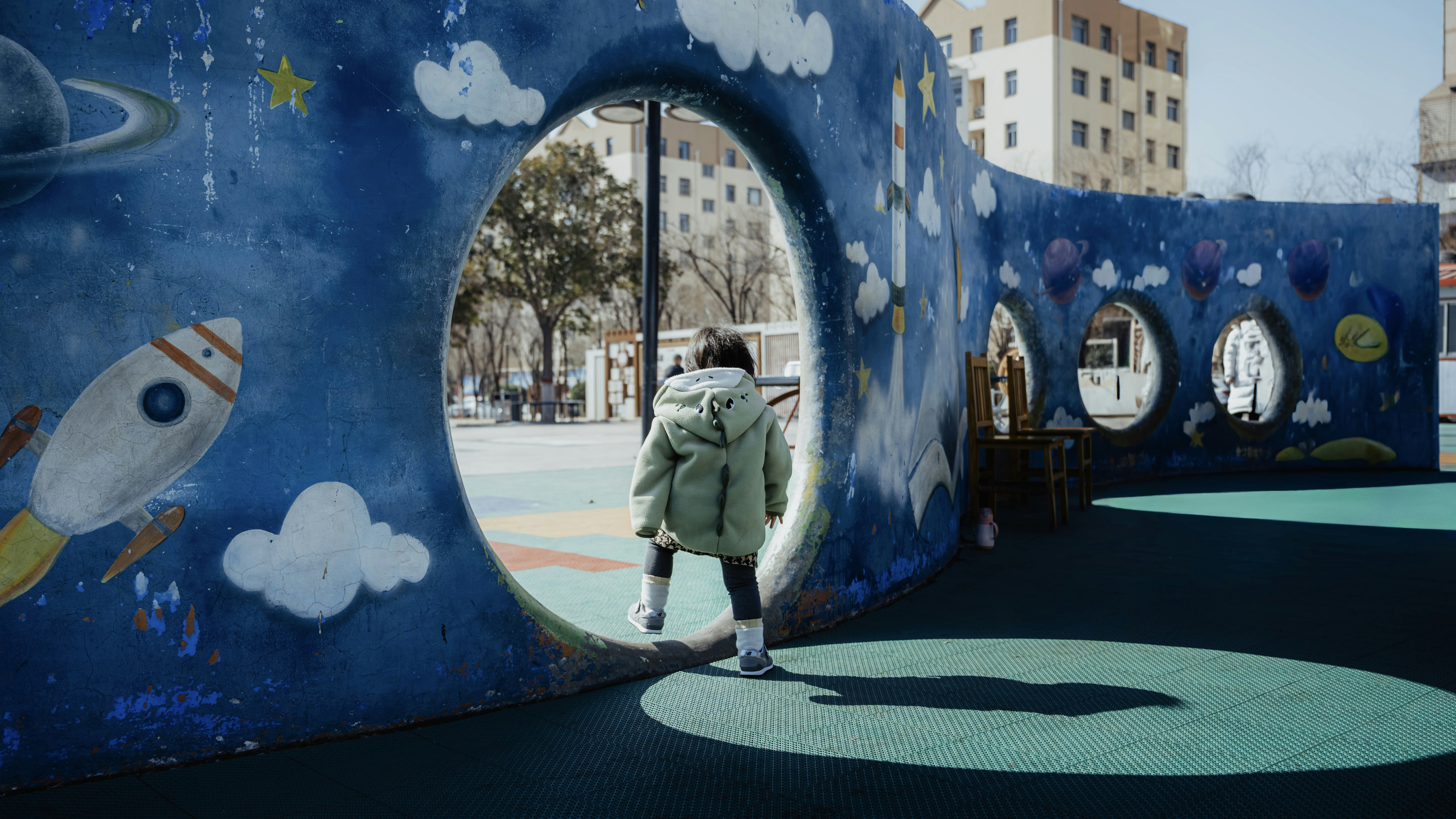 Child walks through a space-themed playground tunnel at play area