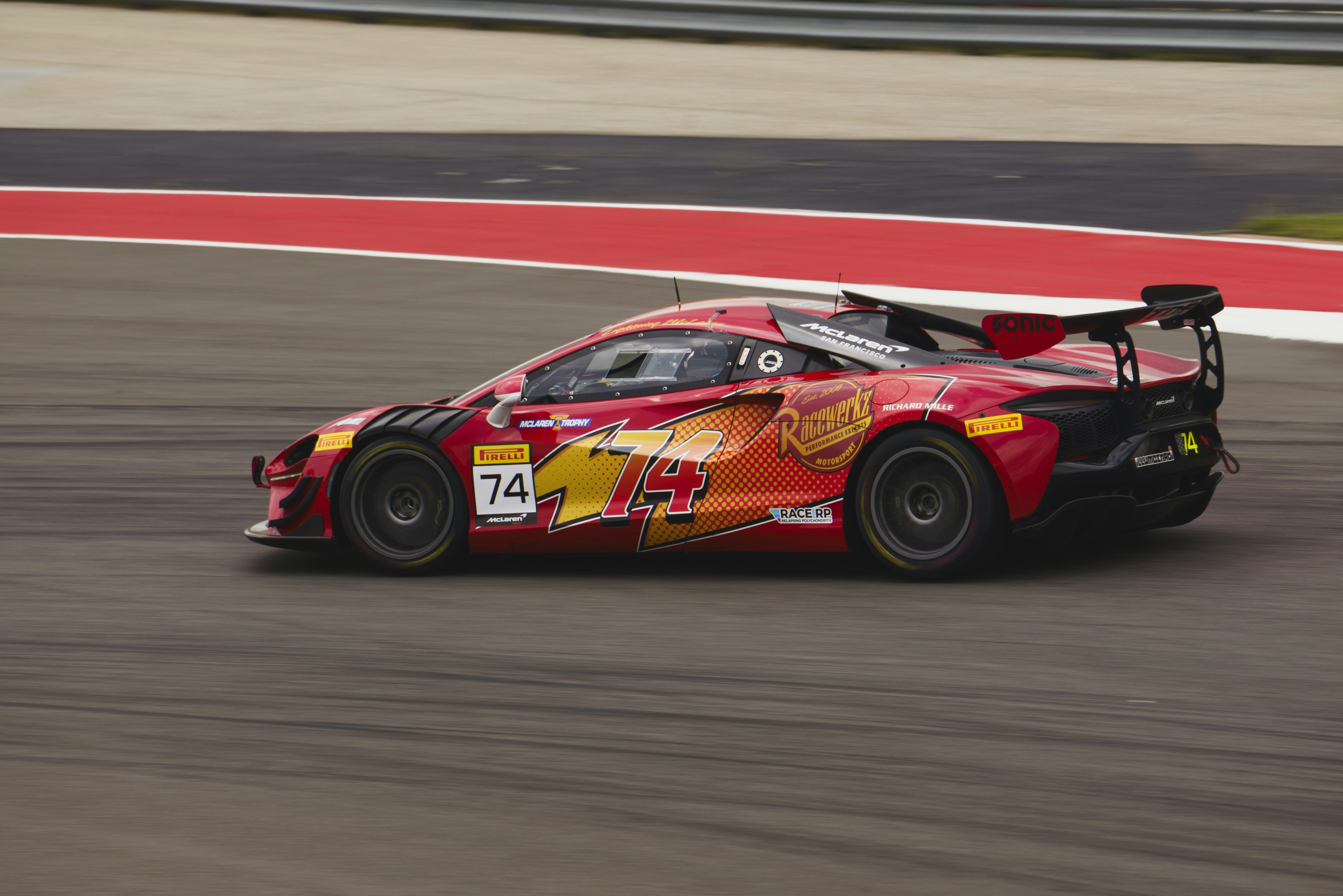 A red race car speeds around a track.