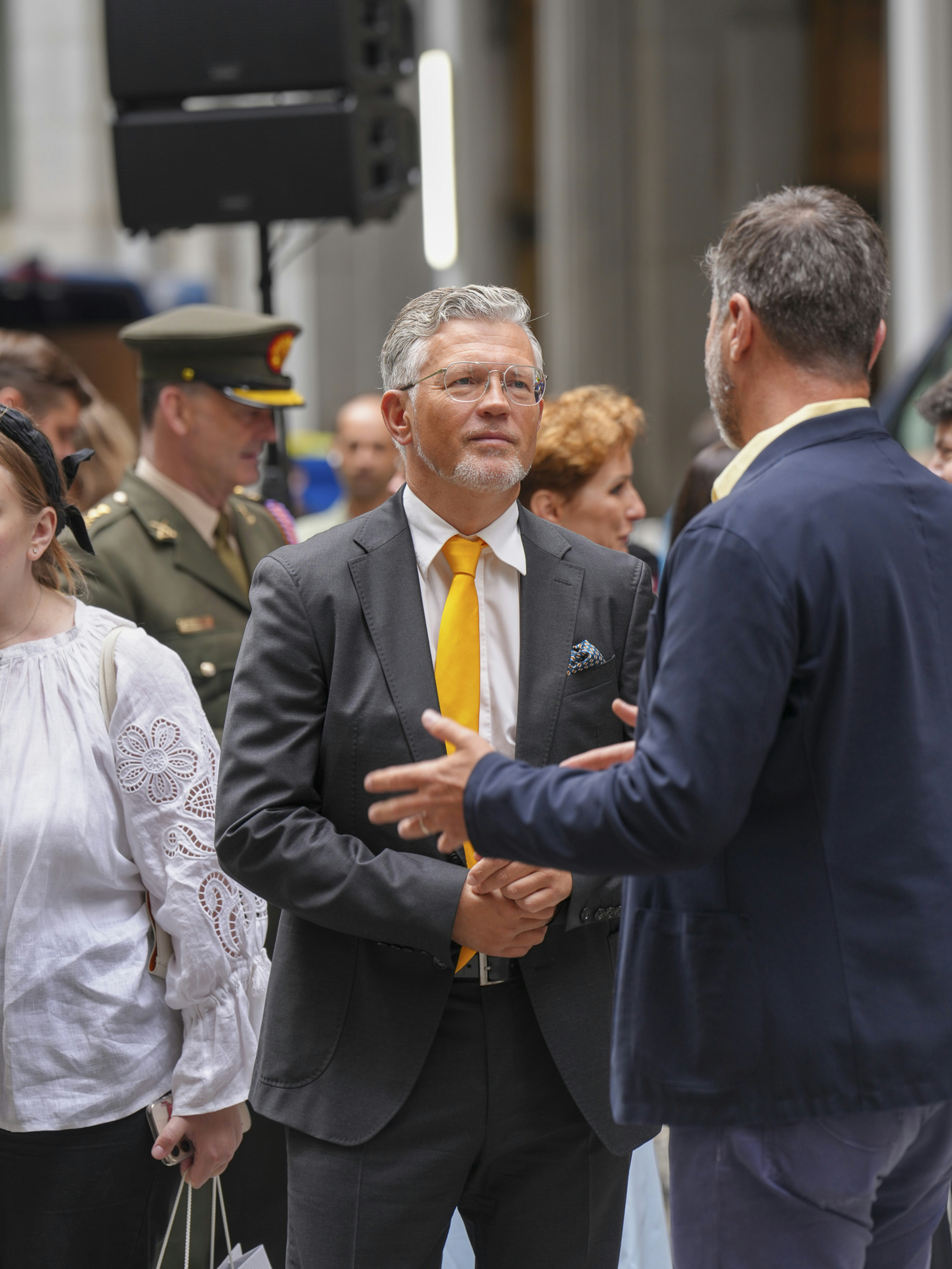 Man in suit talks to another man outdoors.