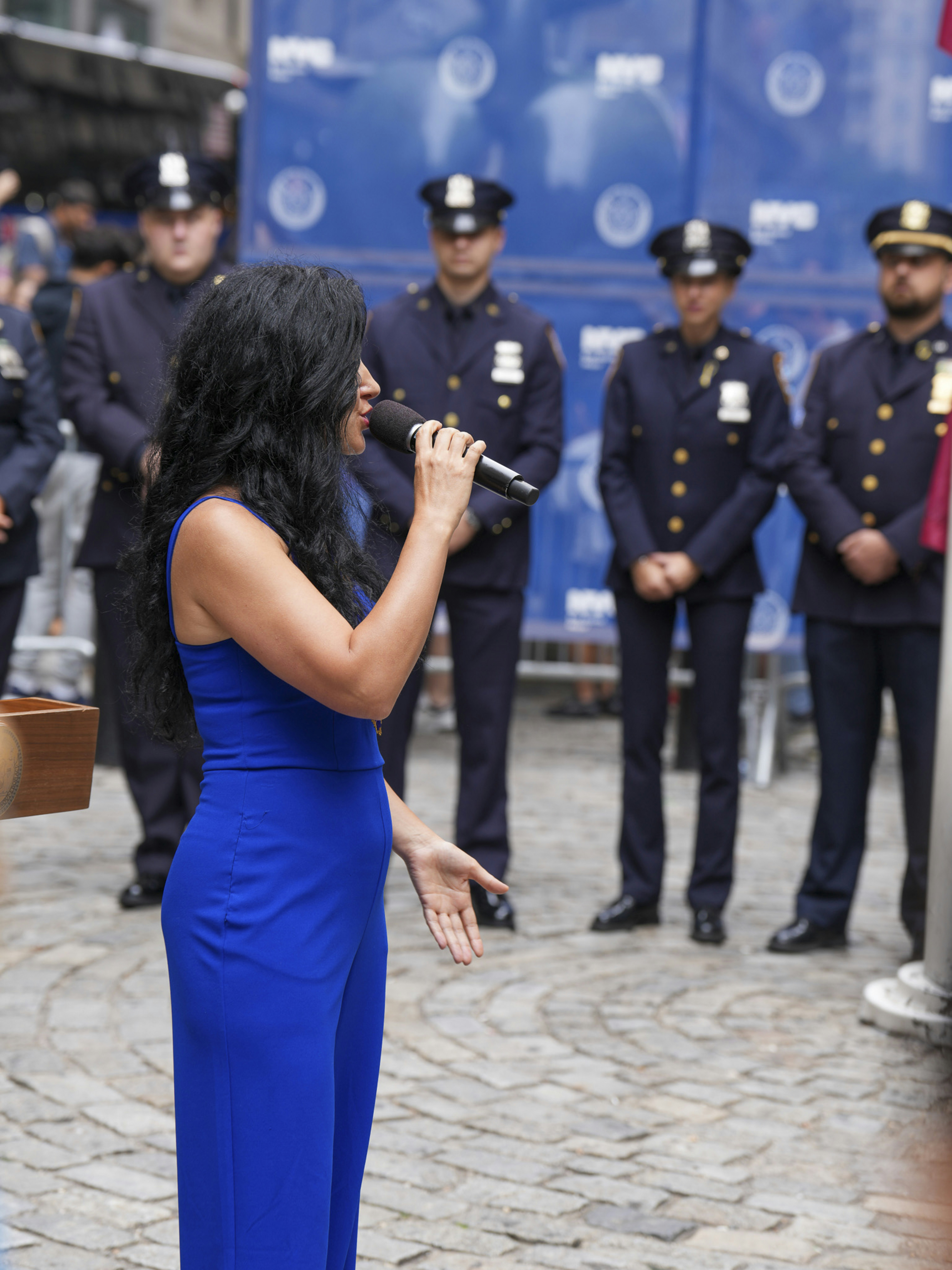 A woman in a blue jumpsuit sings into a microphone.
