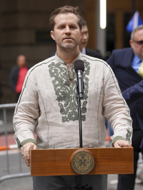 Man in embroidered shirt speaks at podium outdoors podium