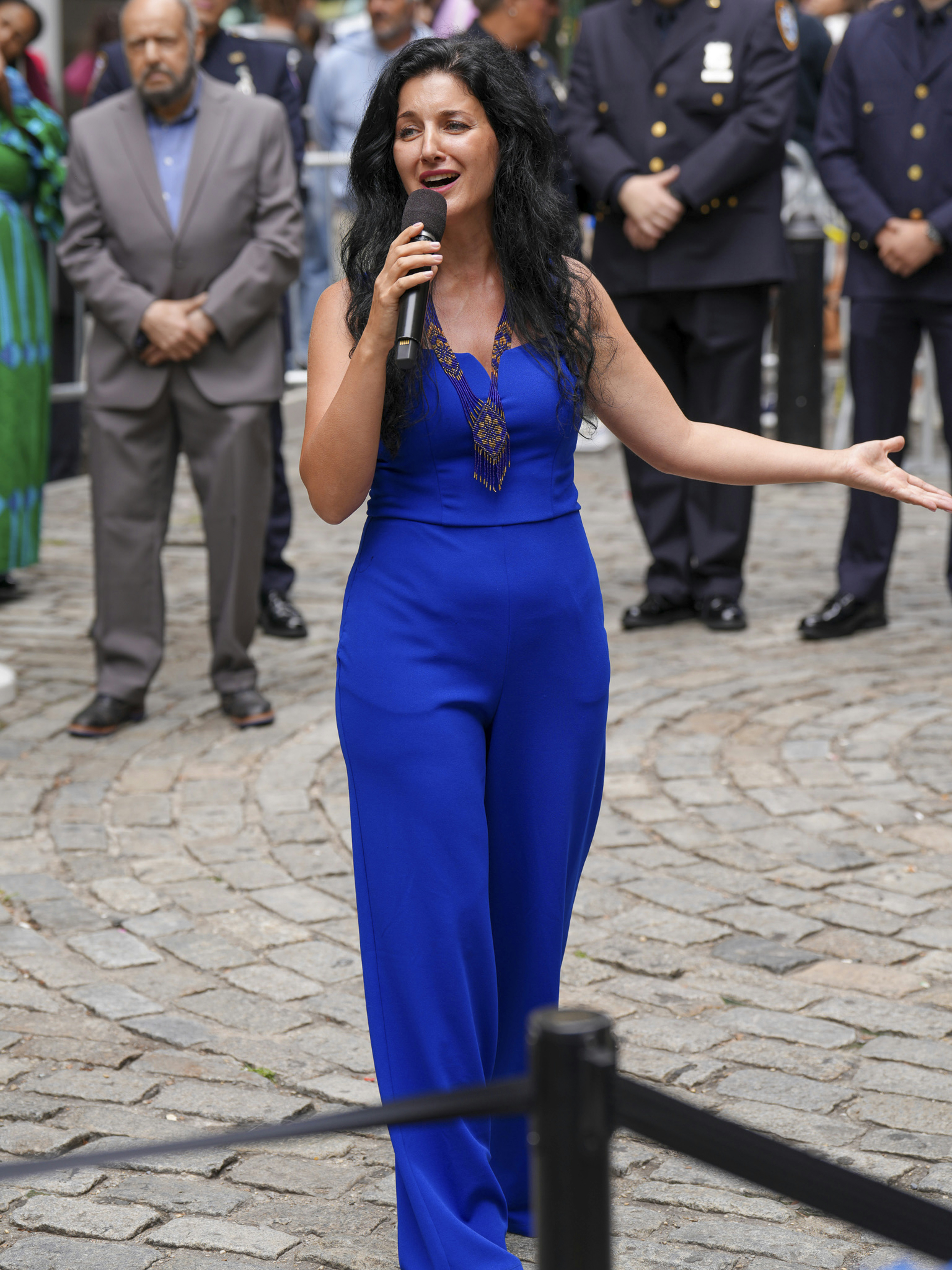 A woman in a blue jumpsuit sings into a microphone.