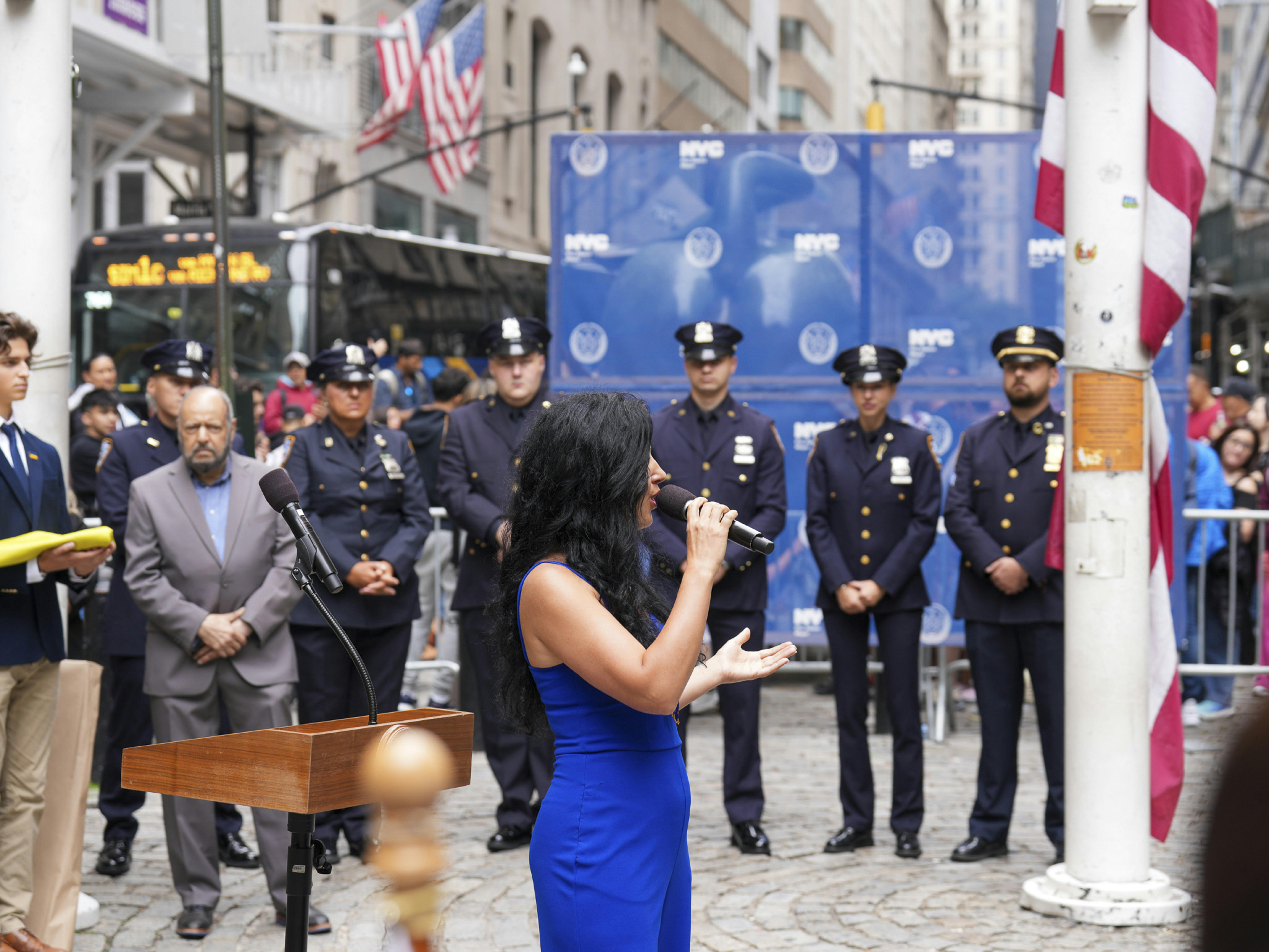 A Ukrainian rally unfolds in downtown Manhattan, where community members, NYC officials, and uniformed police gather in solidarity. A woman draped in a blue and yellow flag stands solemnly among the crowd, while a young attendee holds a folded Ukrainian flag during a formal civic ceremony. The event reflects unity, patriotism, and public support for Ukraine in the heart of New York City. Captured by Olek Buzunov @buzunov.photoart, documenting moments of resilience and civic engagement.