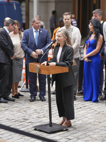 Woman speaks at podium with crowd behind her.