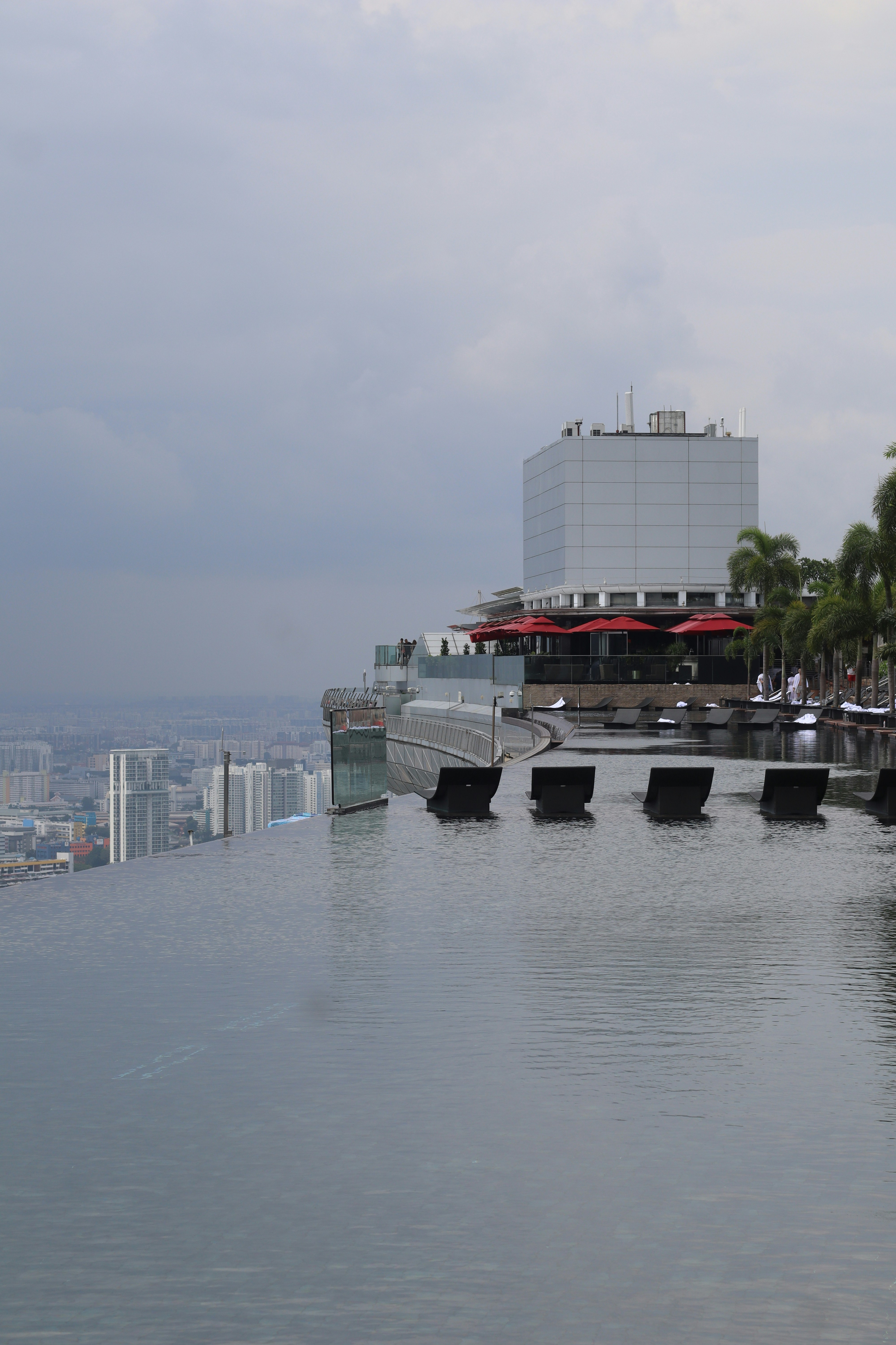 Piscina infinita con vistas a una ciudad en un día nublado.