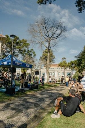 A crowd gathered in a park near a stage surrounded by trees at an evening event