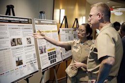 Two people in uniform discuss a presentation board of posters