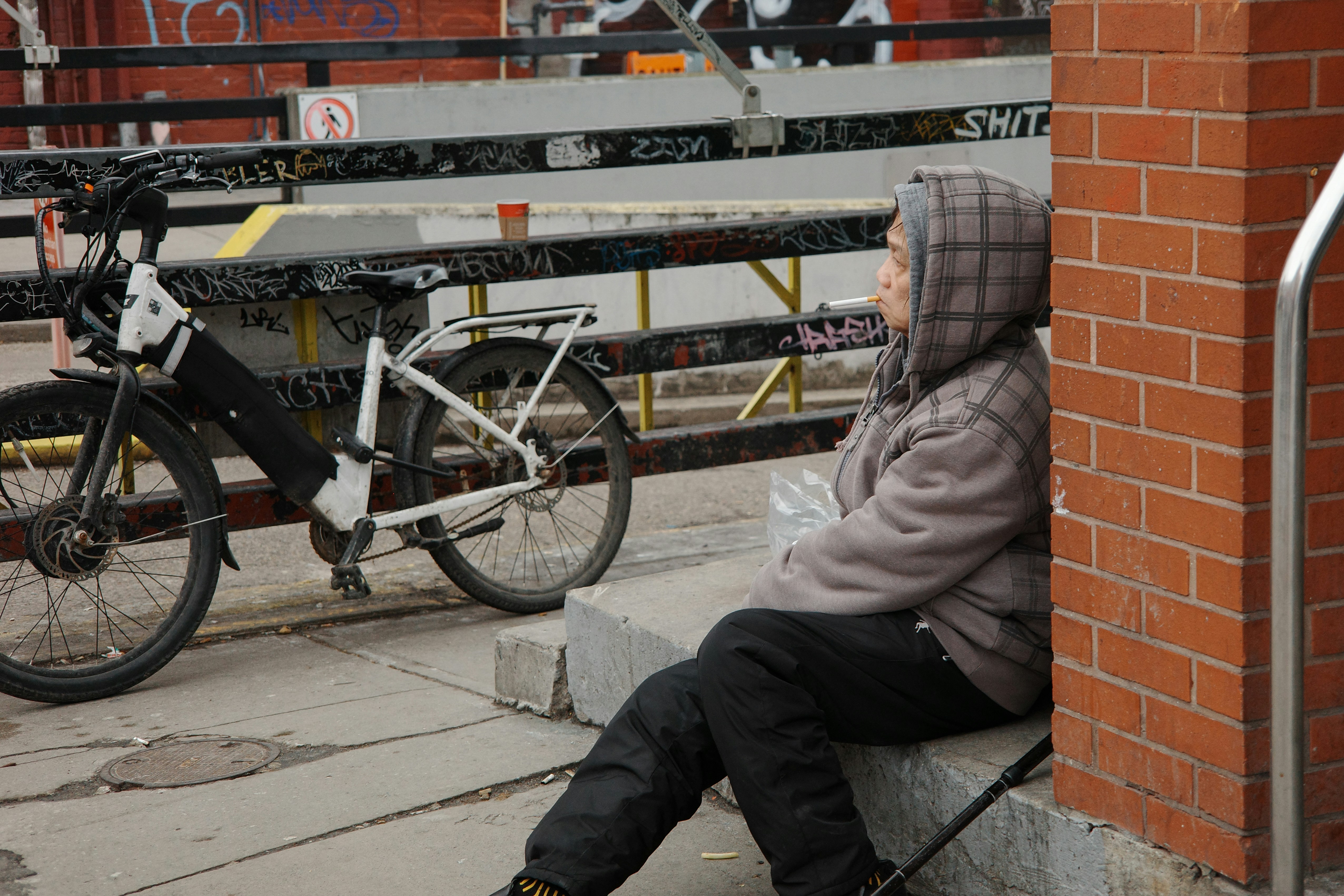 Persona con chaqueta con capucha apoyada en una pared de ladrillo