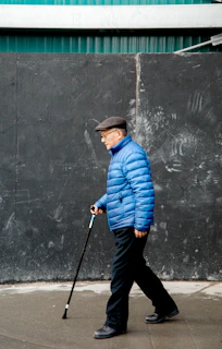 Un homme âgé en veste bleue marche avec une canne.